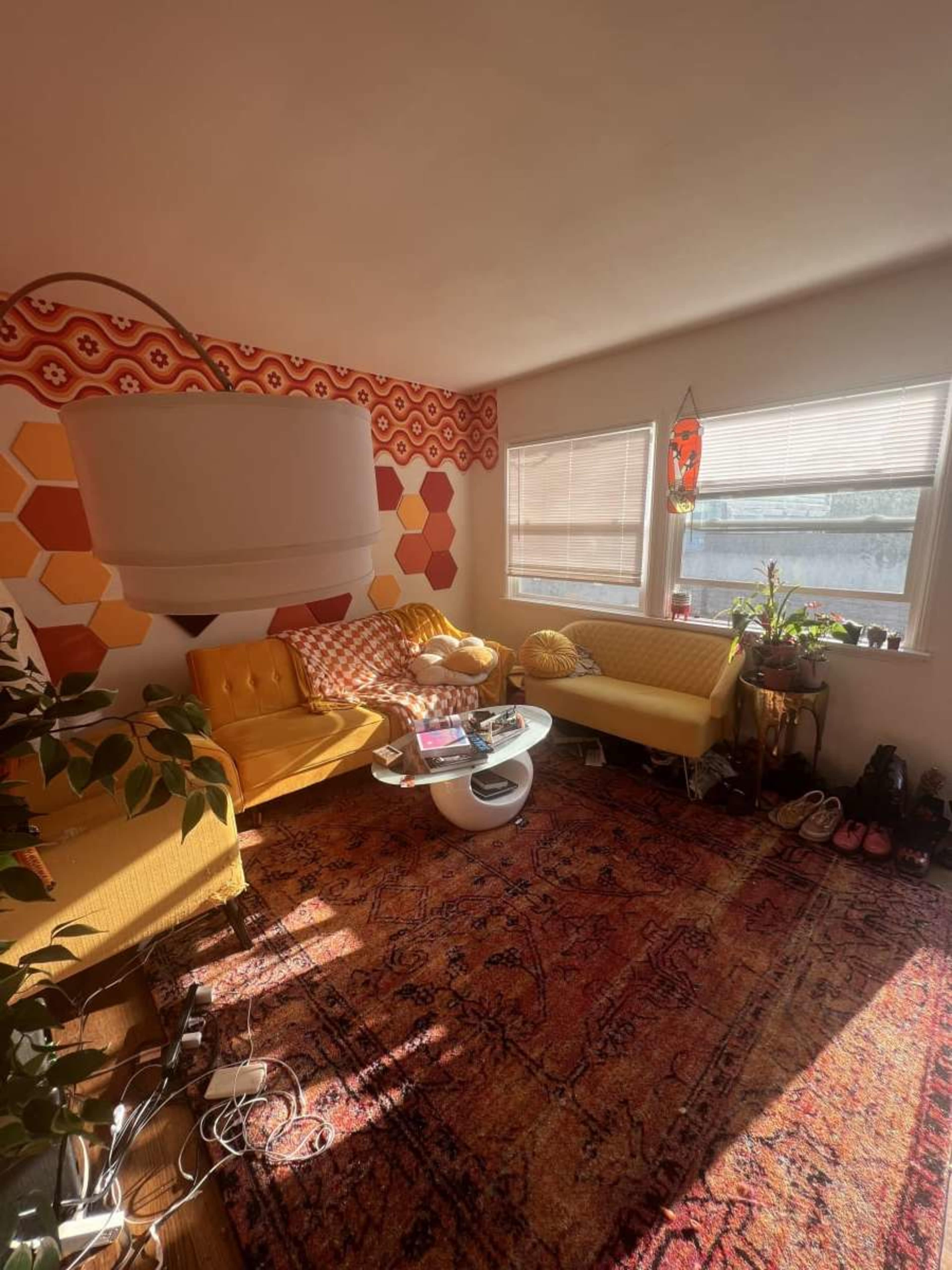 A brightly lit living room featuring yellow sofas, a circular white coffee table, and a patterned rug, with hexagonal designs on the wall.