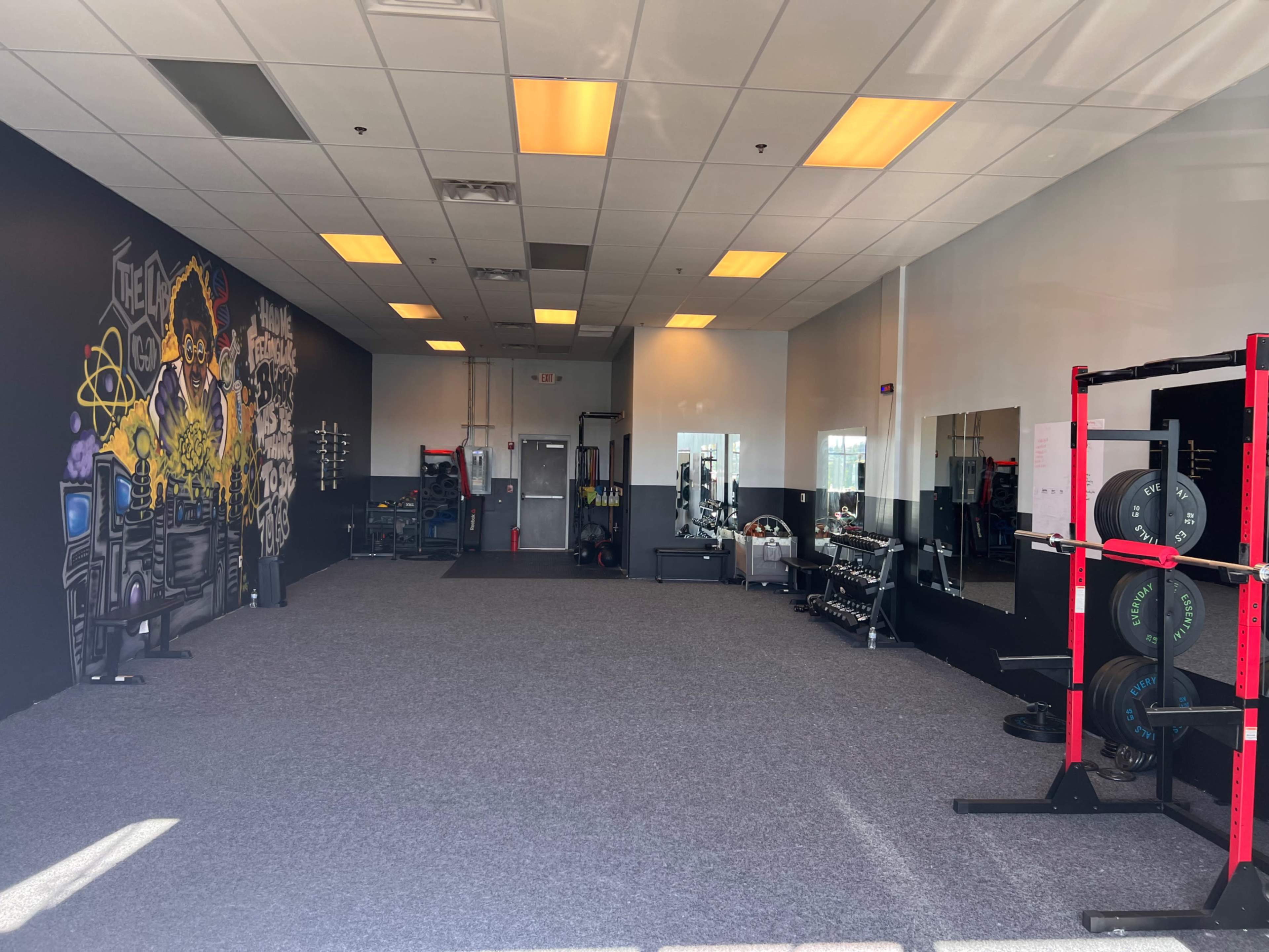 A spacious gym with workout equipment on one side, a mirrored wall, and a colorful mural on the opposite wall.