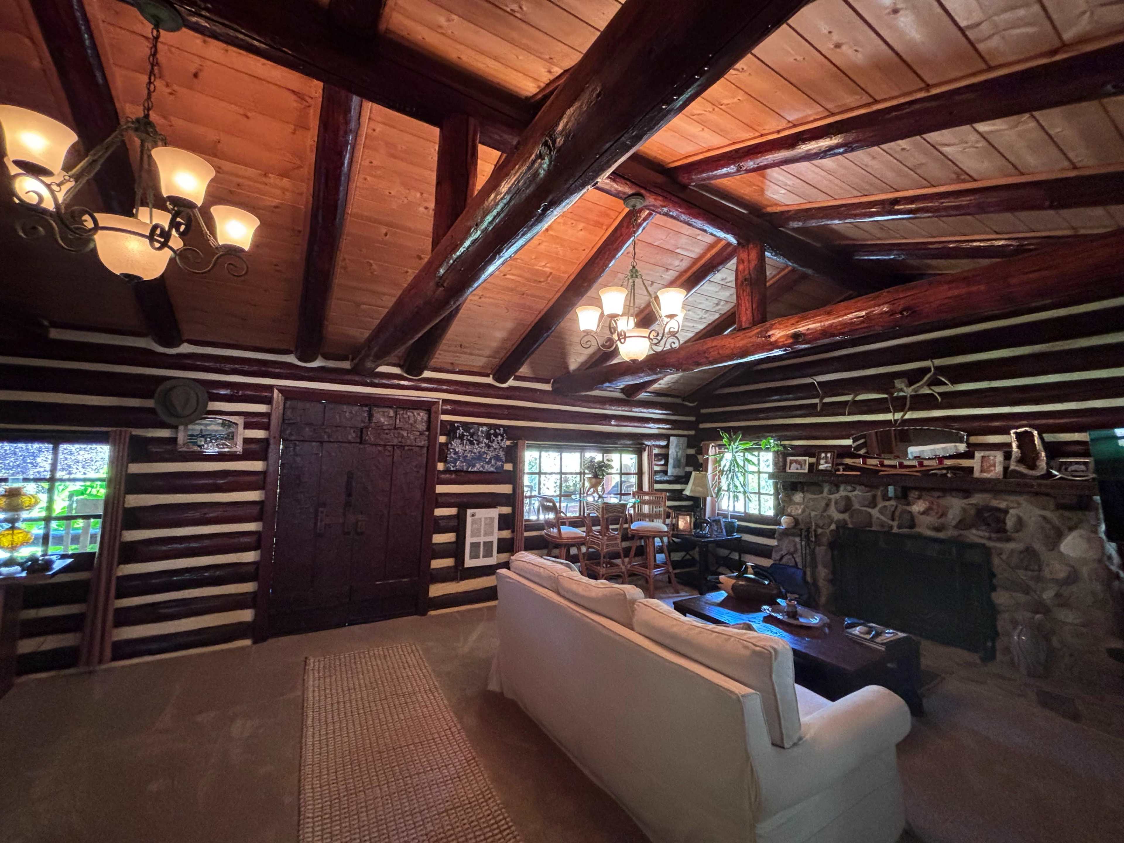 The interior of a rustic log cabin features exposed wooden beams, a stone fireplace, and cozy seating arrangements.