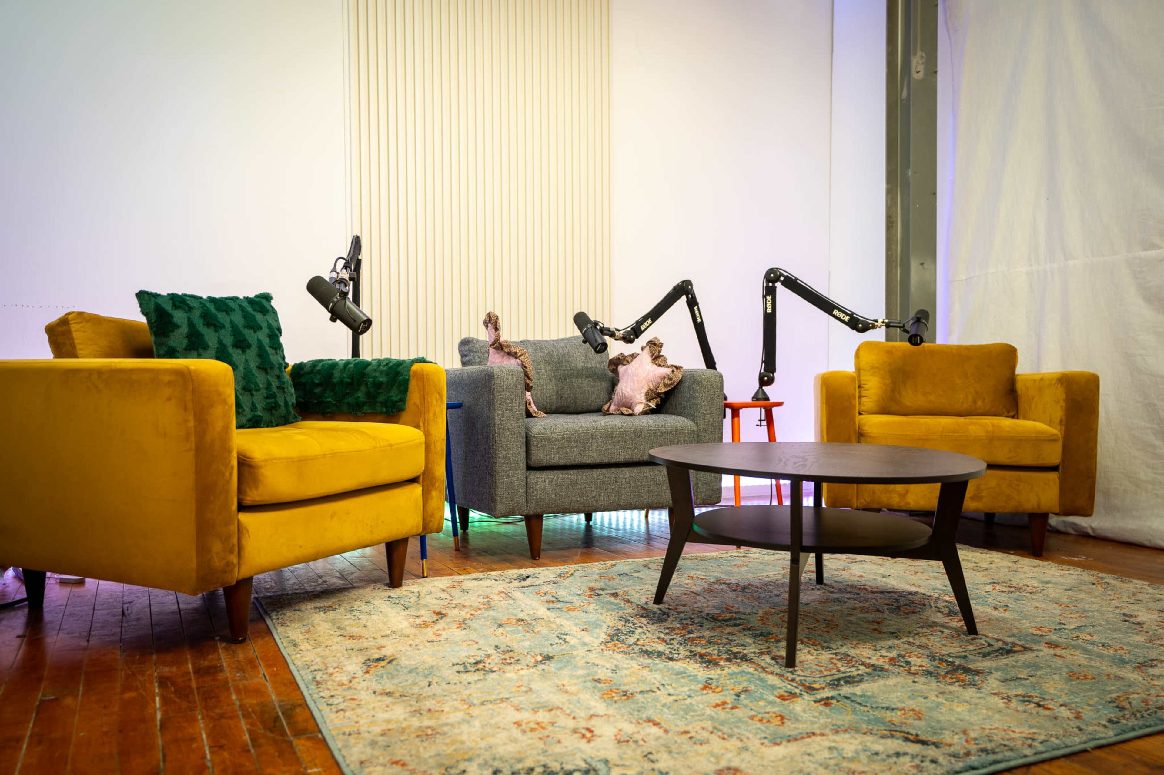 The image shows a cozy seating area with two colorful armchairs and a round coffee table, set against a backdrop of studio equipment.