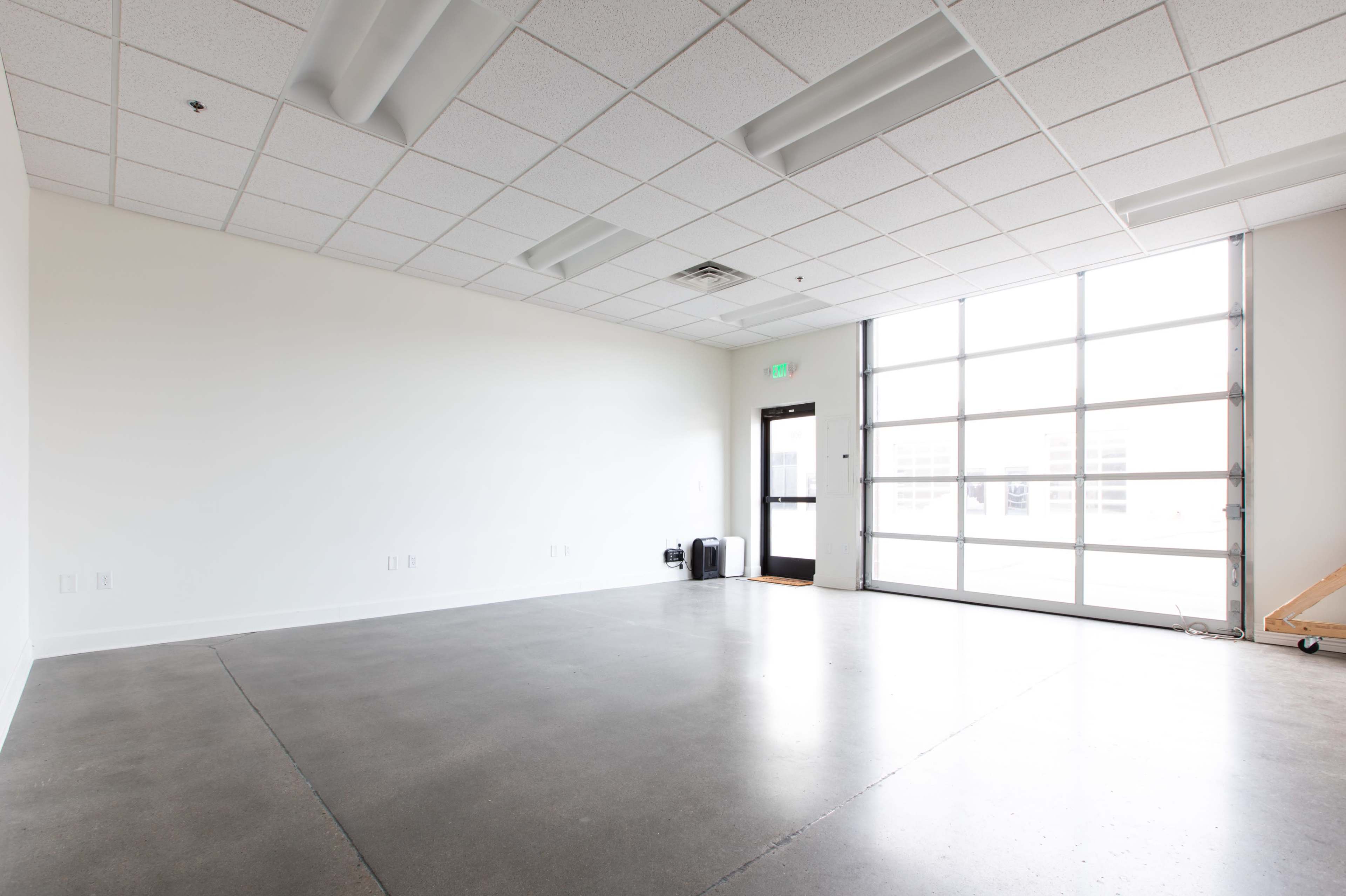 An empty room with a concrete floor, a large window, and a door leading outside.