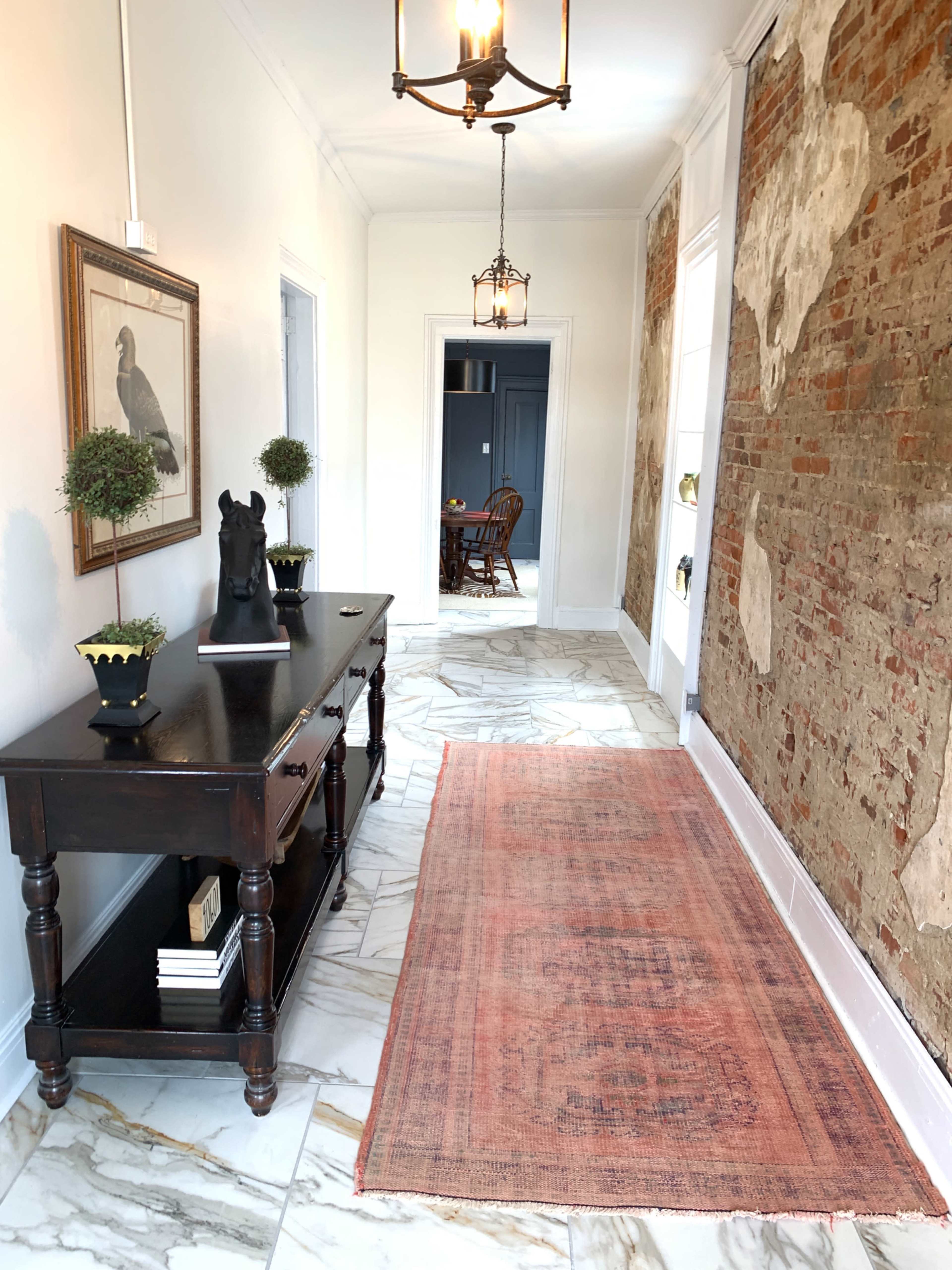 A hallway featuring a wooden console table, a decorative rug, and exposed brick walls.