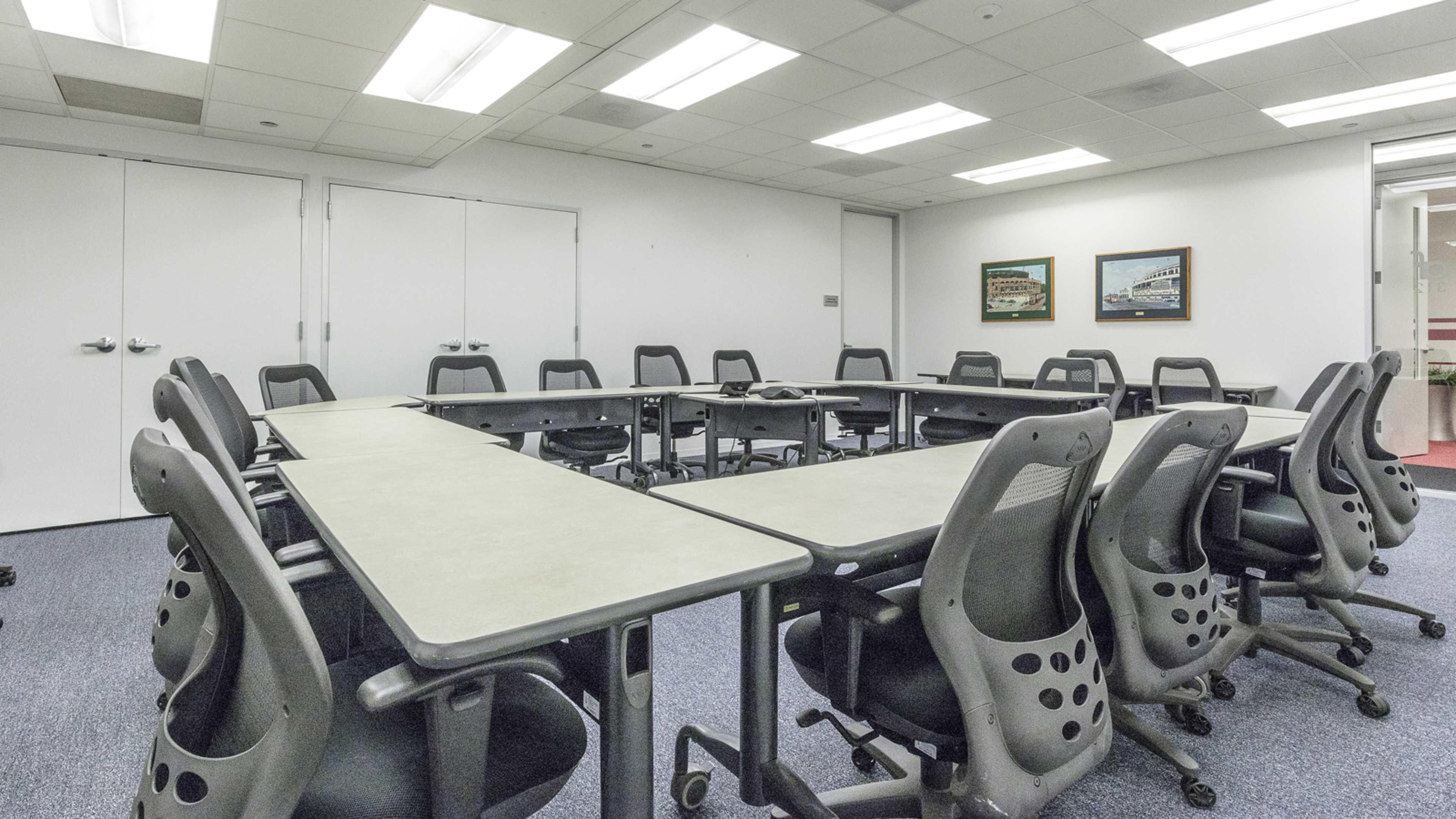 A large conference room features a rectangular table surrounded by ergonomic chairs, with two framed pictures mounted on the wall.