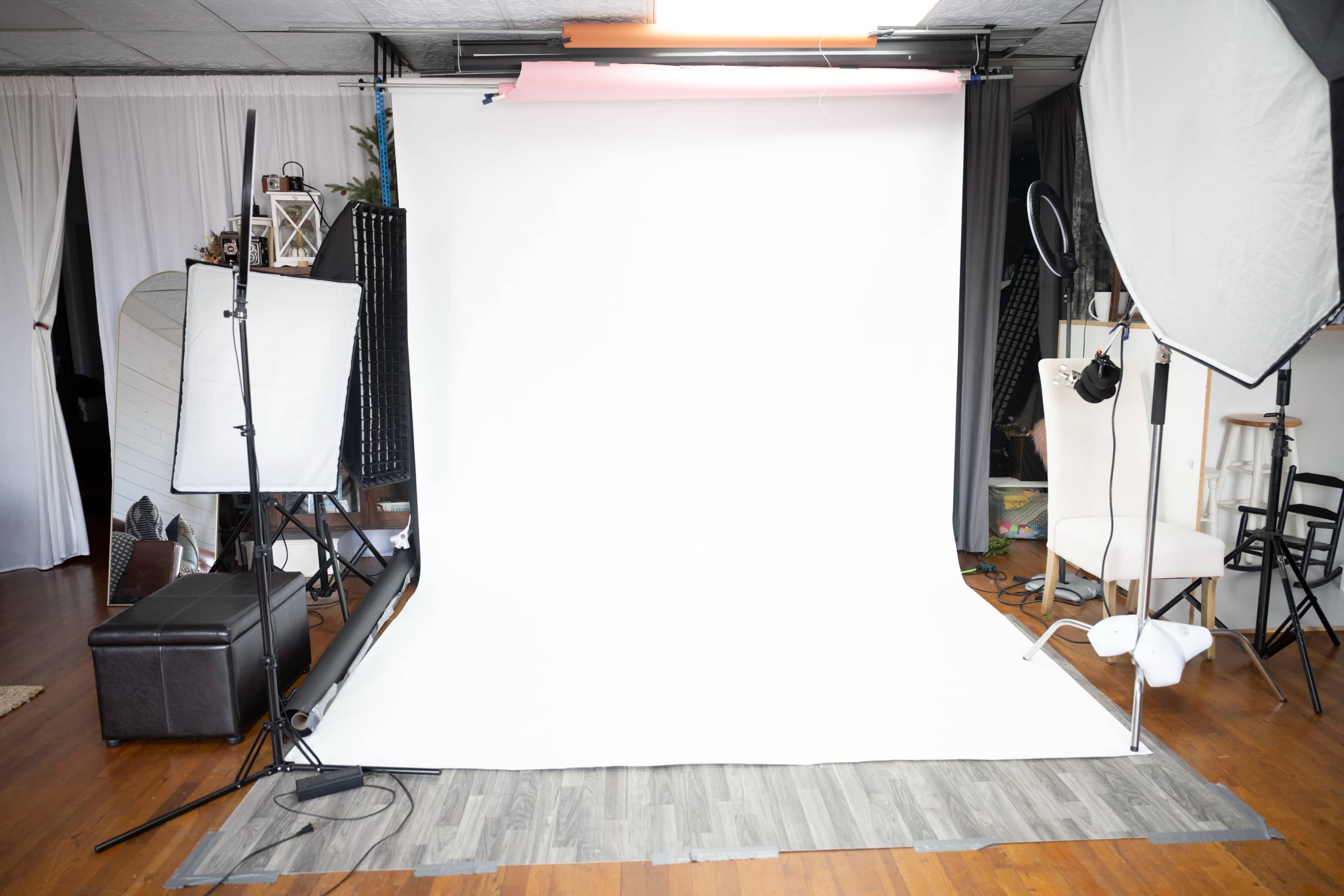 The image shows a photography studio setup with a white backdrop, lighting equipment, and props arranged in a spacious setting.