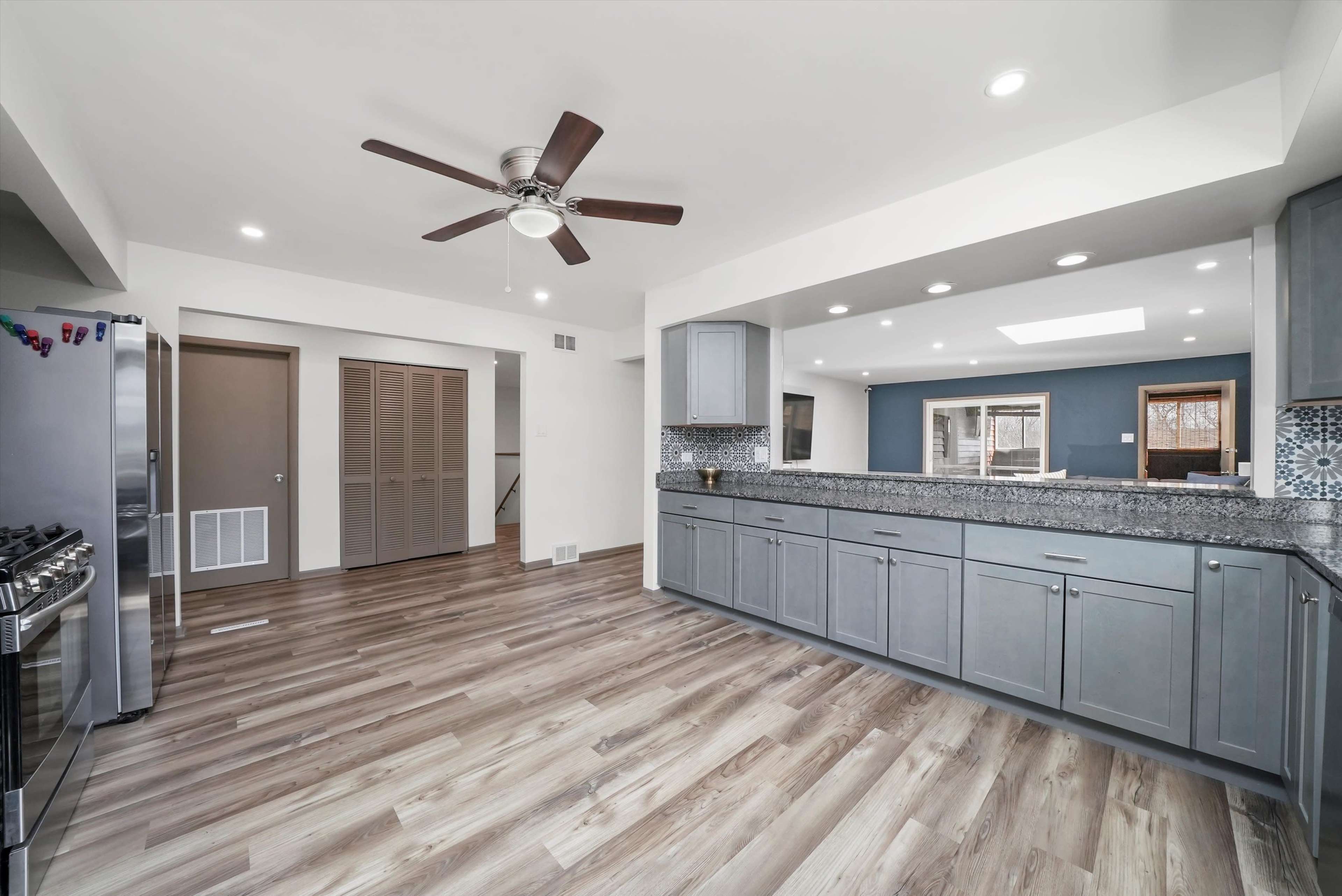 A modern kitchen featuring gray cabinets, a large countertop, stainless steel appliances, and a ceiling fan.