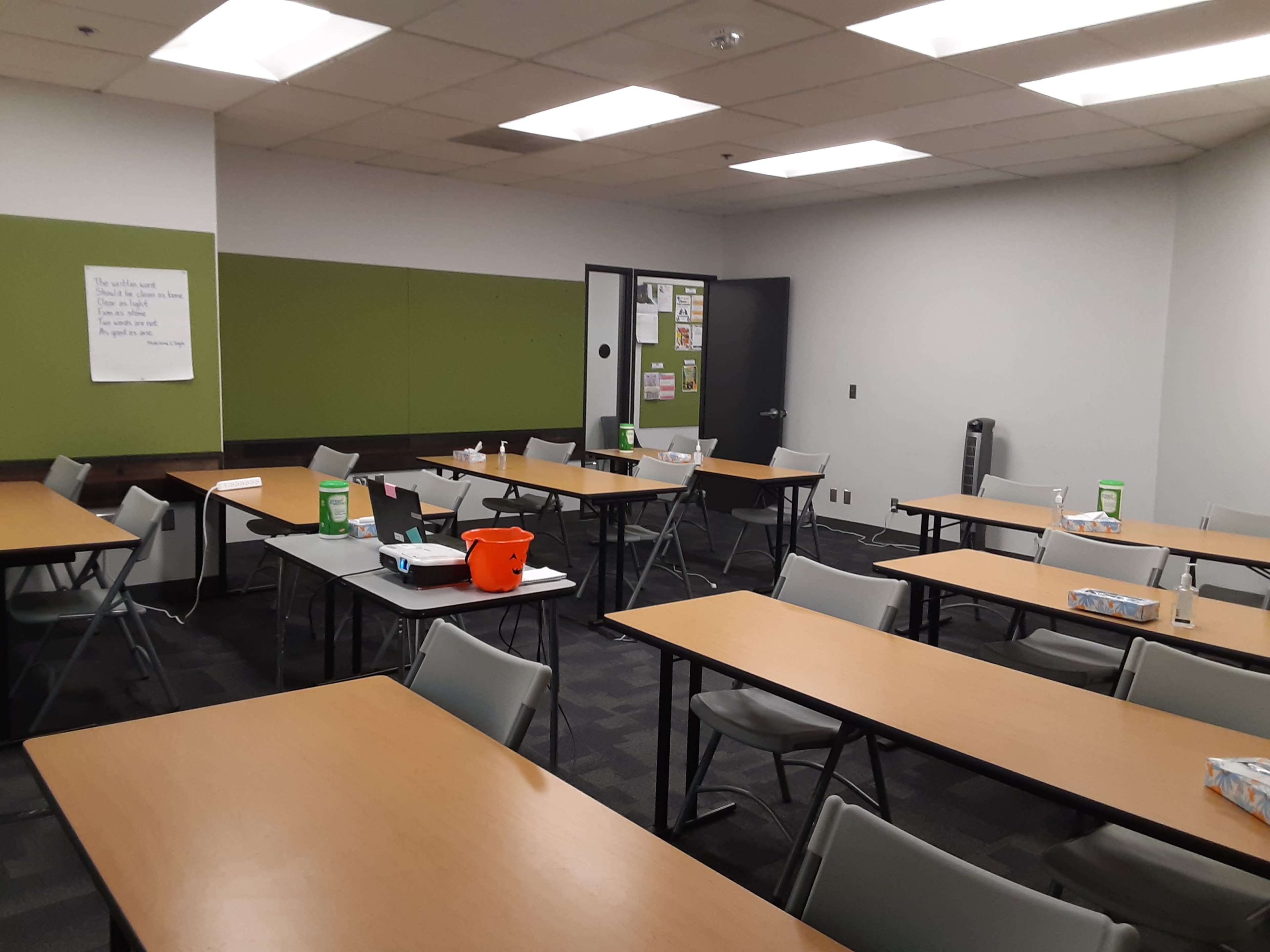 A classroom with multiple tables and chairs arranged in the space, along with supplies and a whiteboard on the wall.