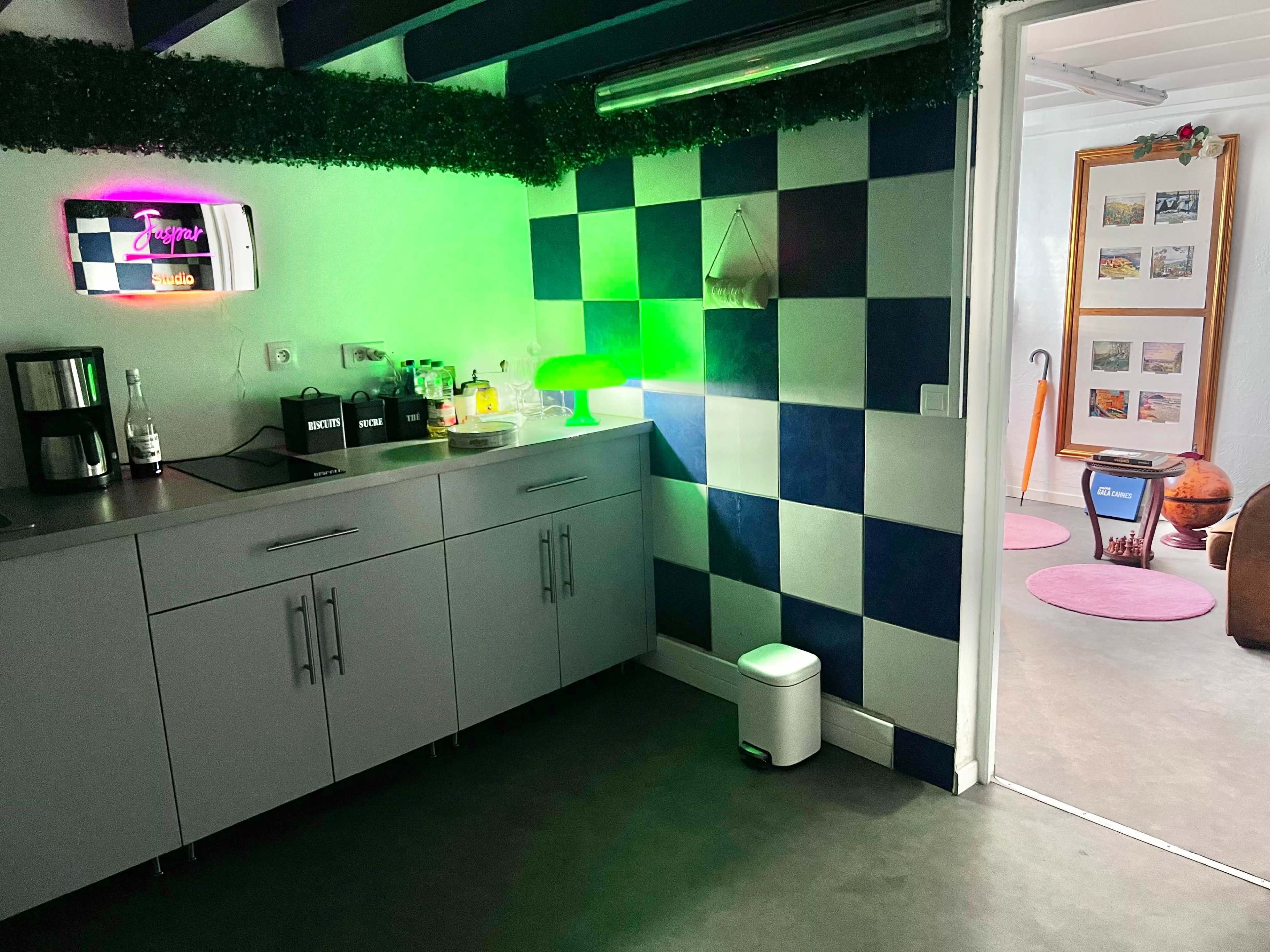 The image shows a modern kitchen area with blue and white checkered walls, a countertop with various kitchen appliances, and illuminated decor creating a vibrant atmosphere.