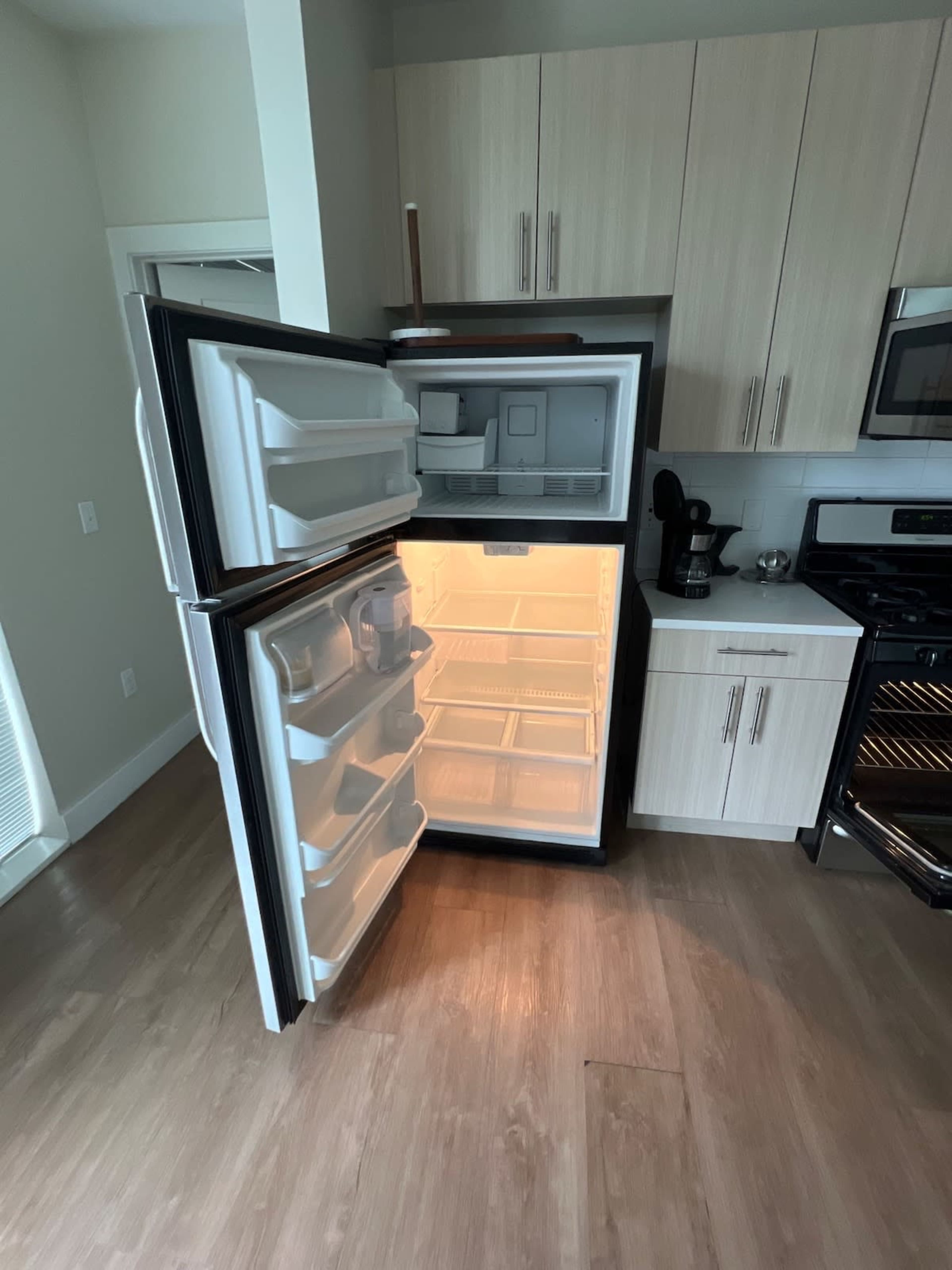 The image shows an open refrigerator with empty shelves, located in a kitchen with modern cabinetry and appliances.