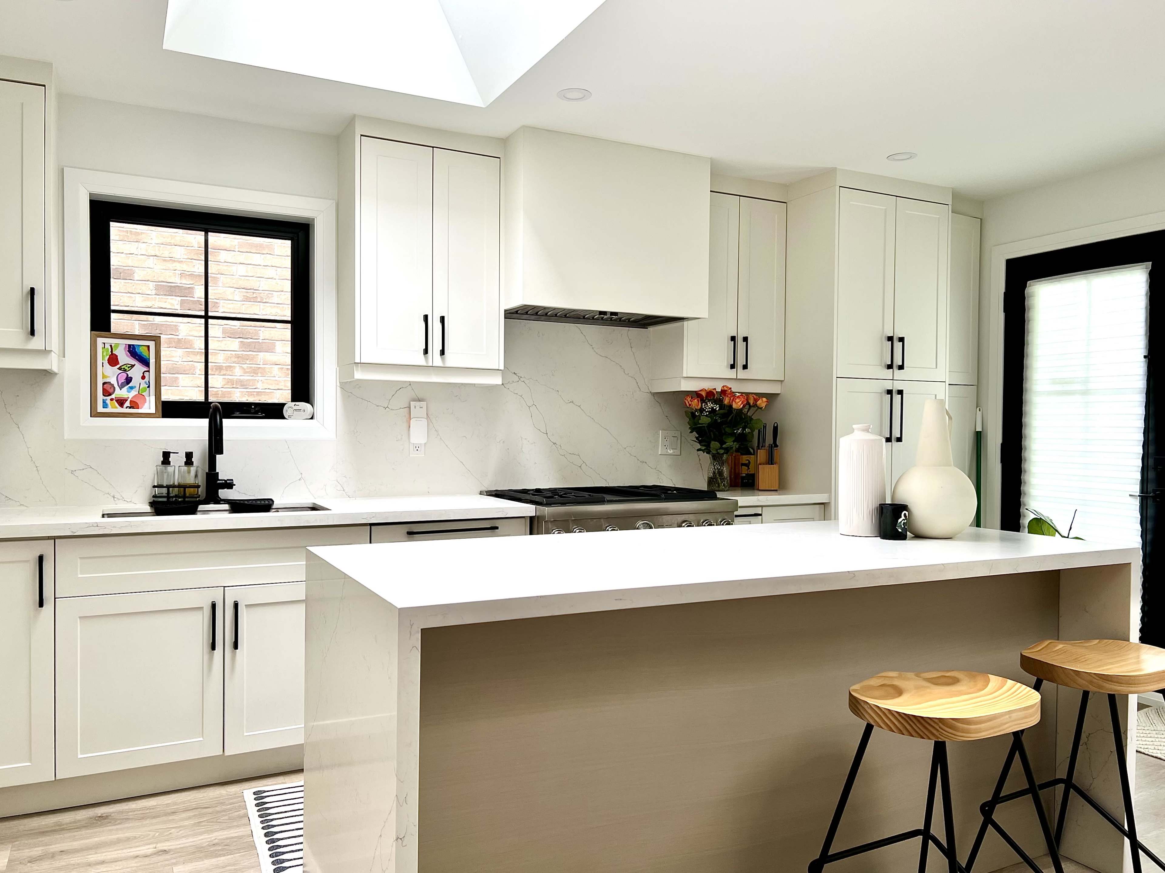 The image shows a modern kitchen with white cabinetry, a large island, and wooden bar stools.
