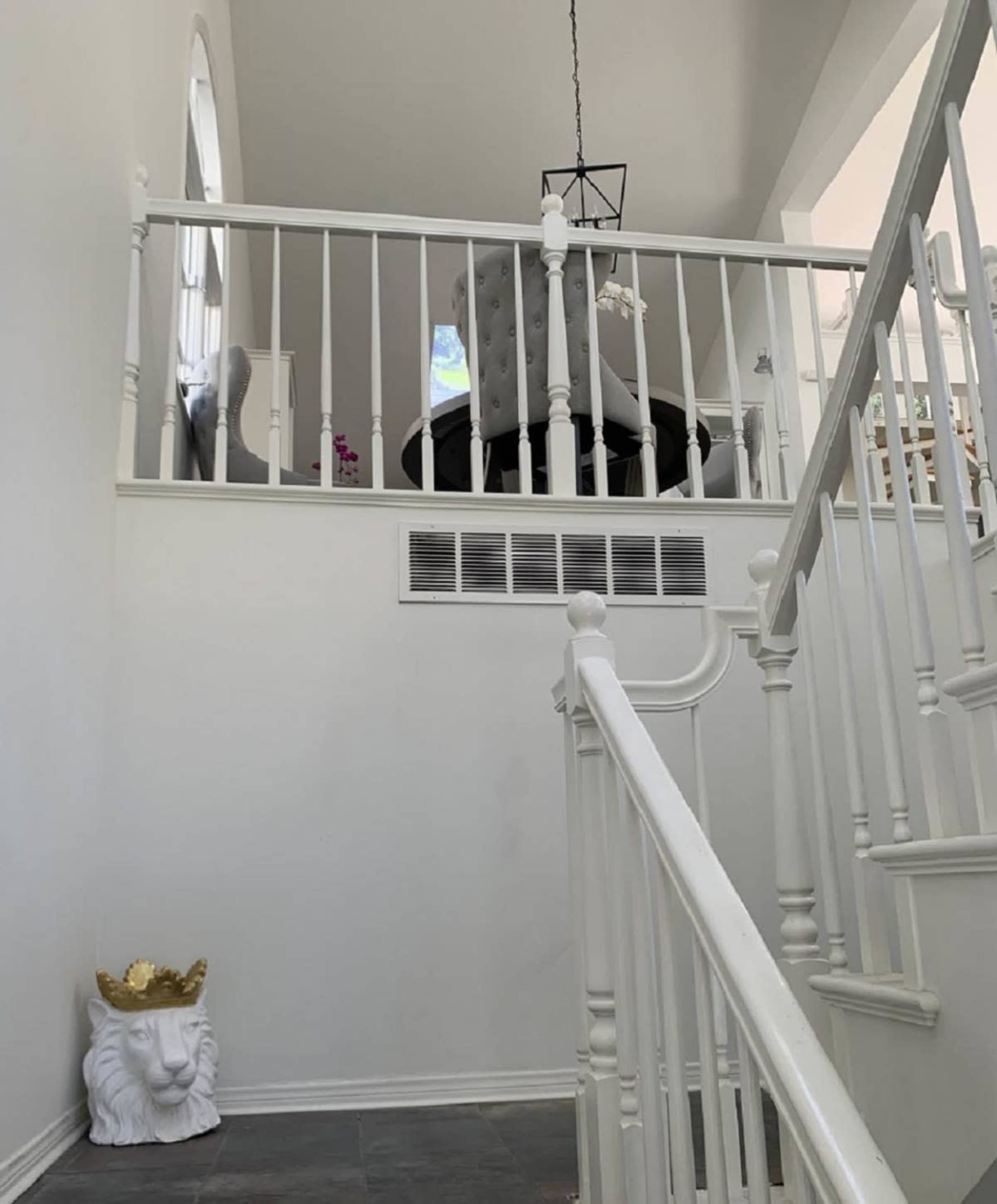A stairway leading to an upper floor with a lion-shaped sculpture at the base and a gray chair visible in the background.