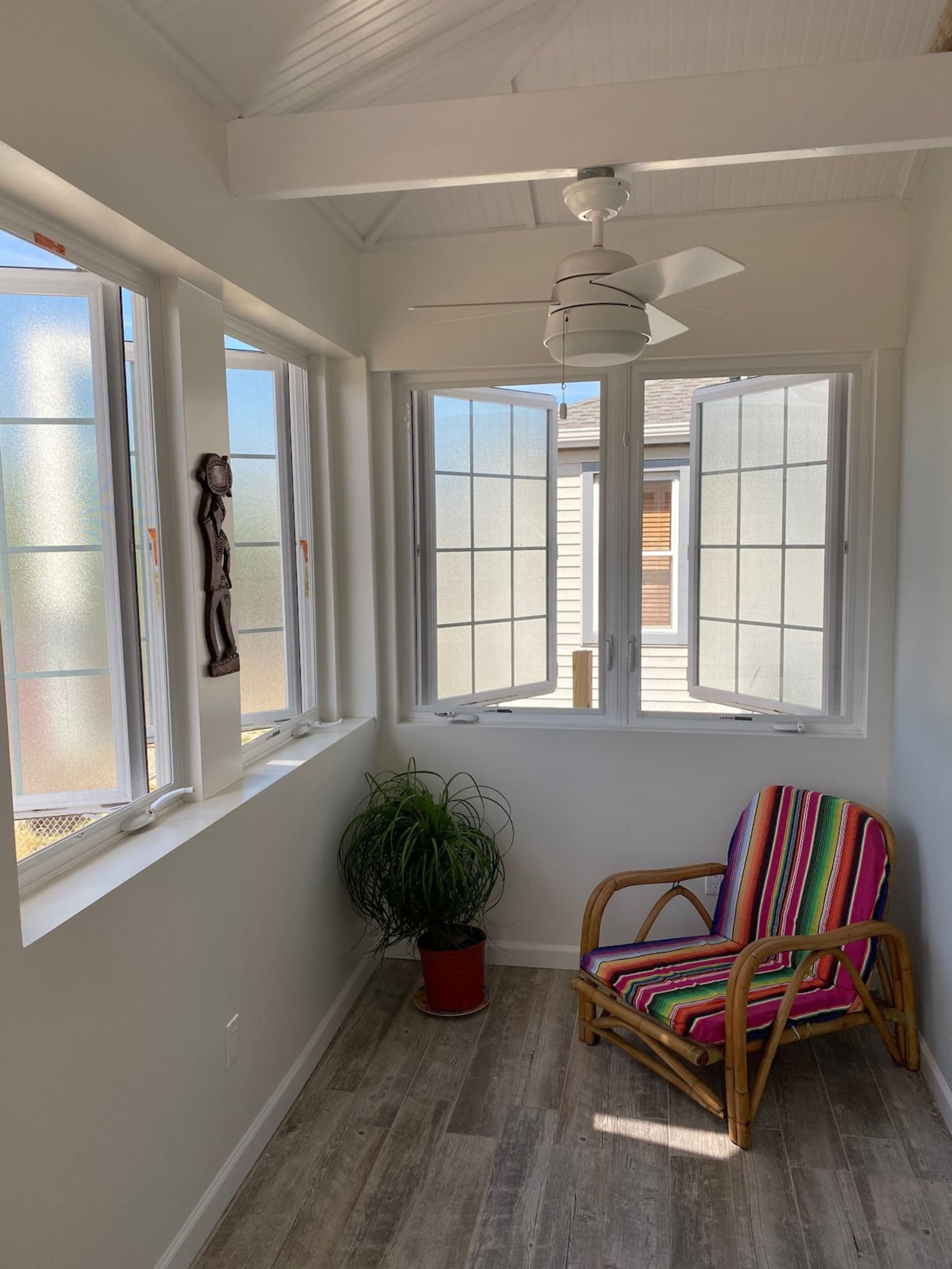 A brightly lit corner of a room features a colorful chair, a potted plant, and open windows that allow natural light to enter.