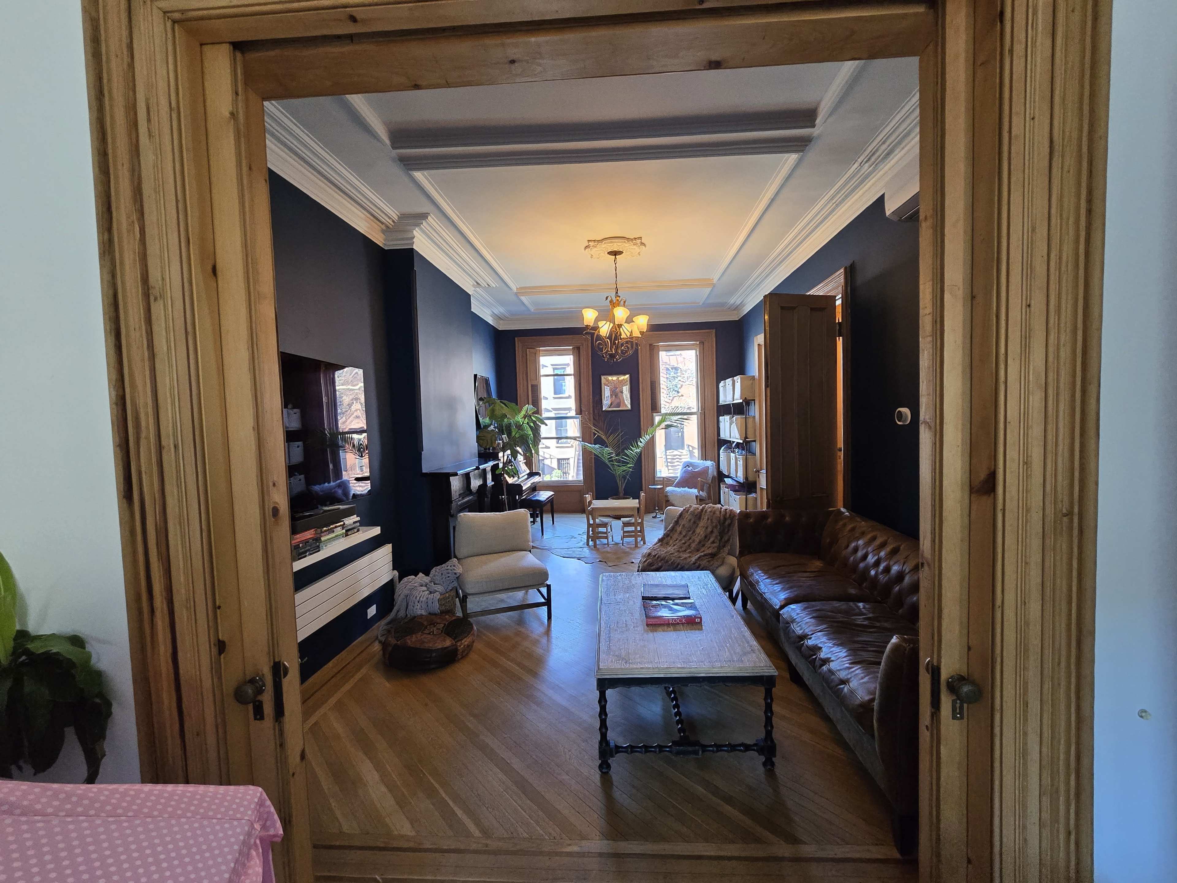 A view from a hallway shows a living room with dark walls, a leather sofa, a wooden coffee table, and a chandelier.
