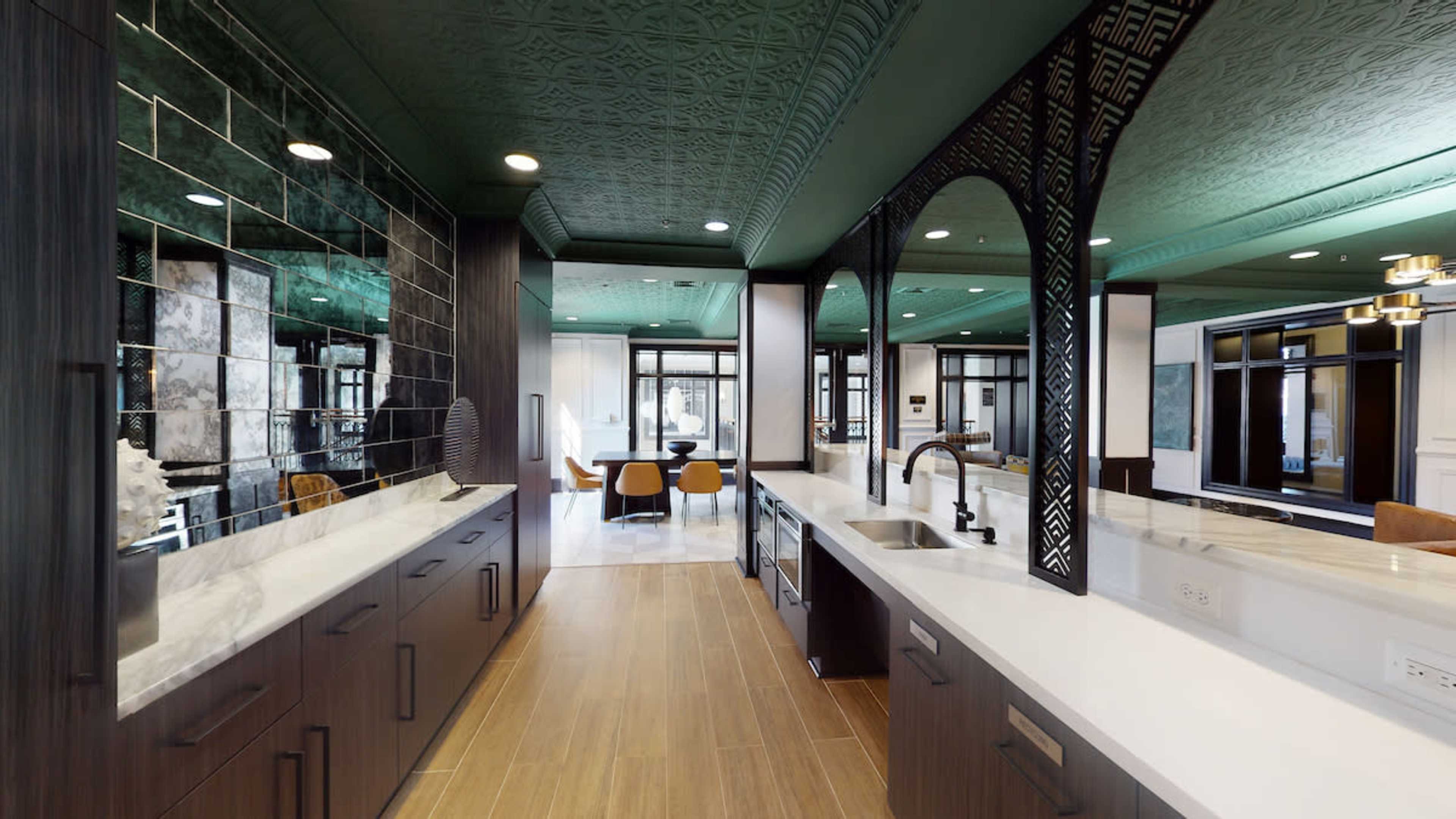 A modern kitchen with dark cabinetry, white countertops, and an elaborate green ceiling design.