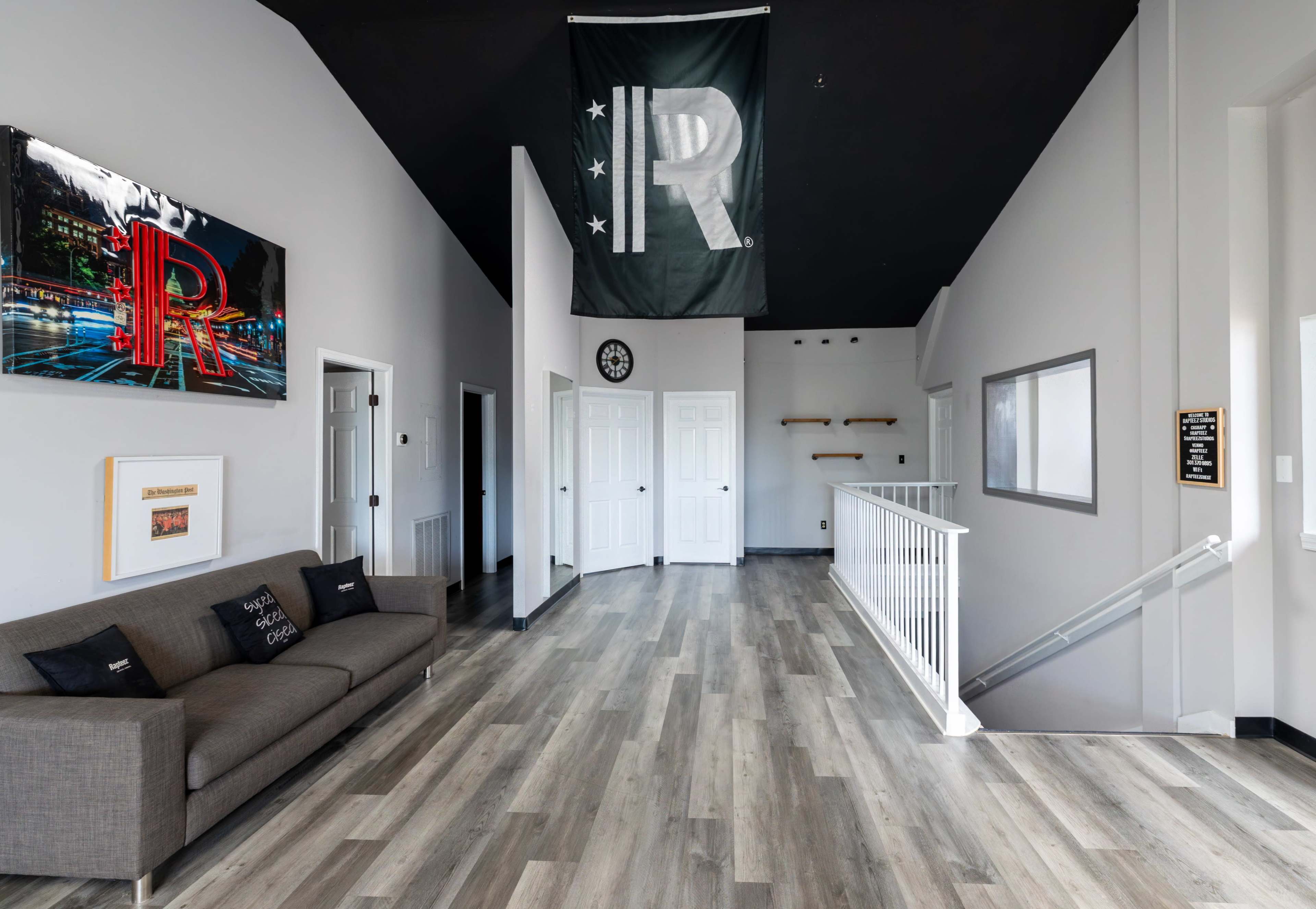 The image shows a modern interior hallway featuring a gray sofa, a large flag hanging from the ceiling, and double doors leading to other rooms.