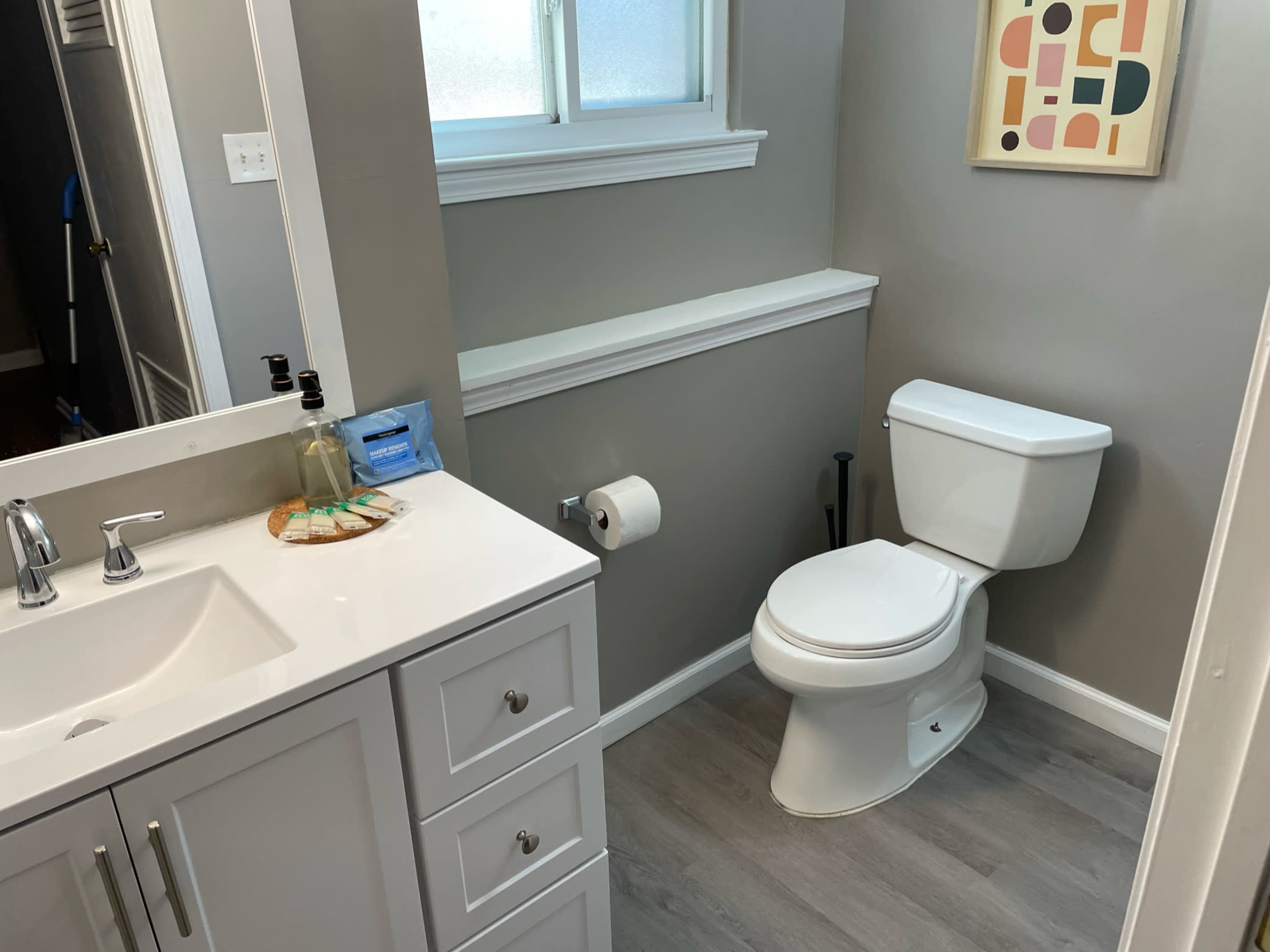 A bathroom with a white toilet, a sink with a mirror, and a window letting in natural light.