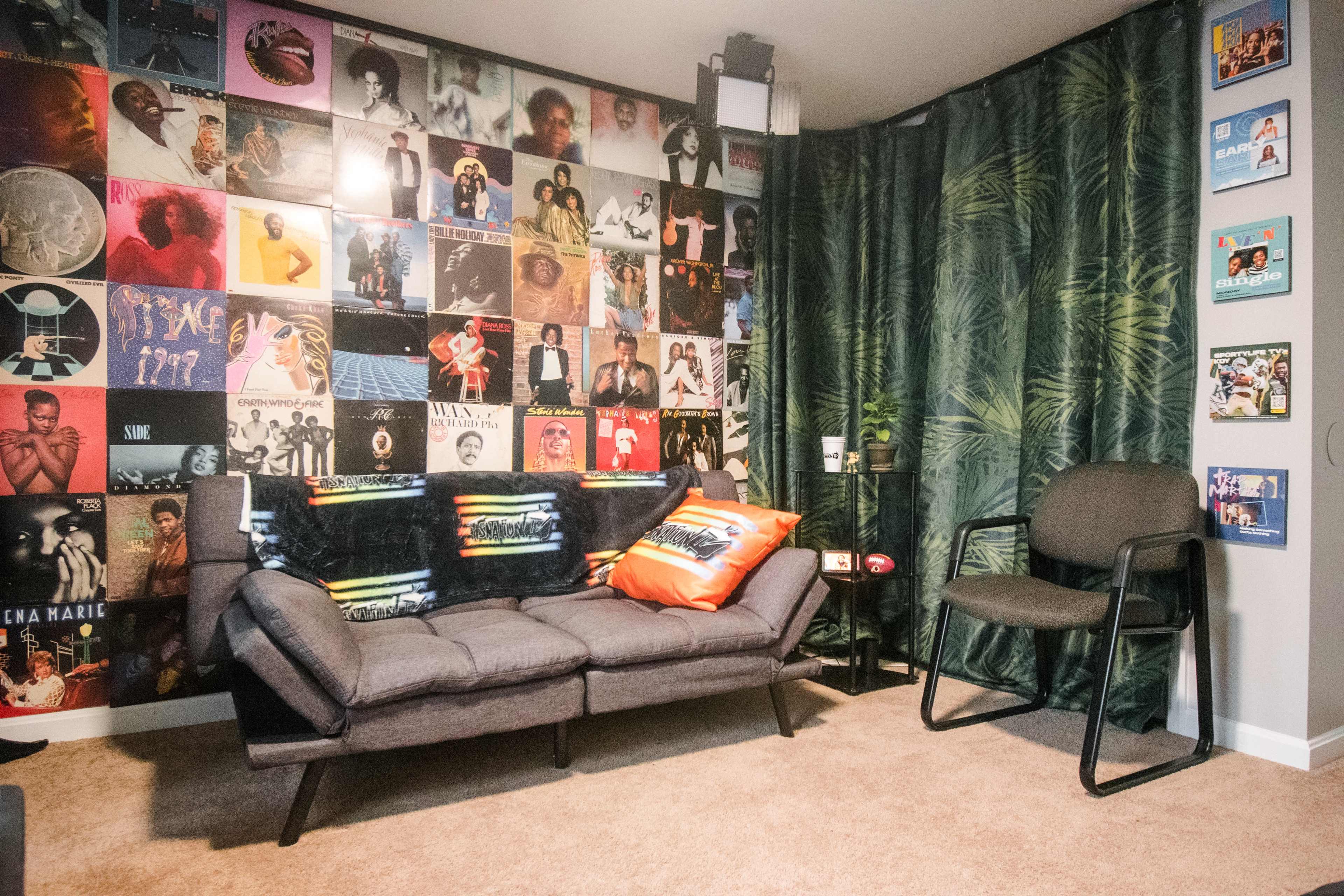 A cozy living room with a sofa decorated with colorful pillows, surrounded by a wall covered in framed vintage record album covers and a small side table.