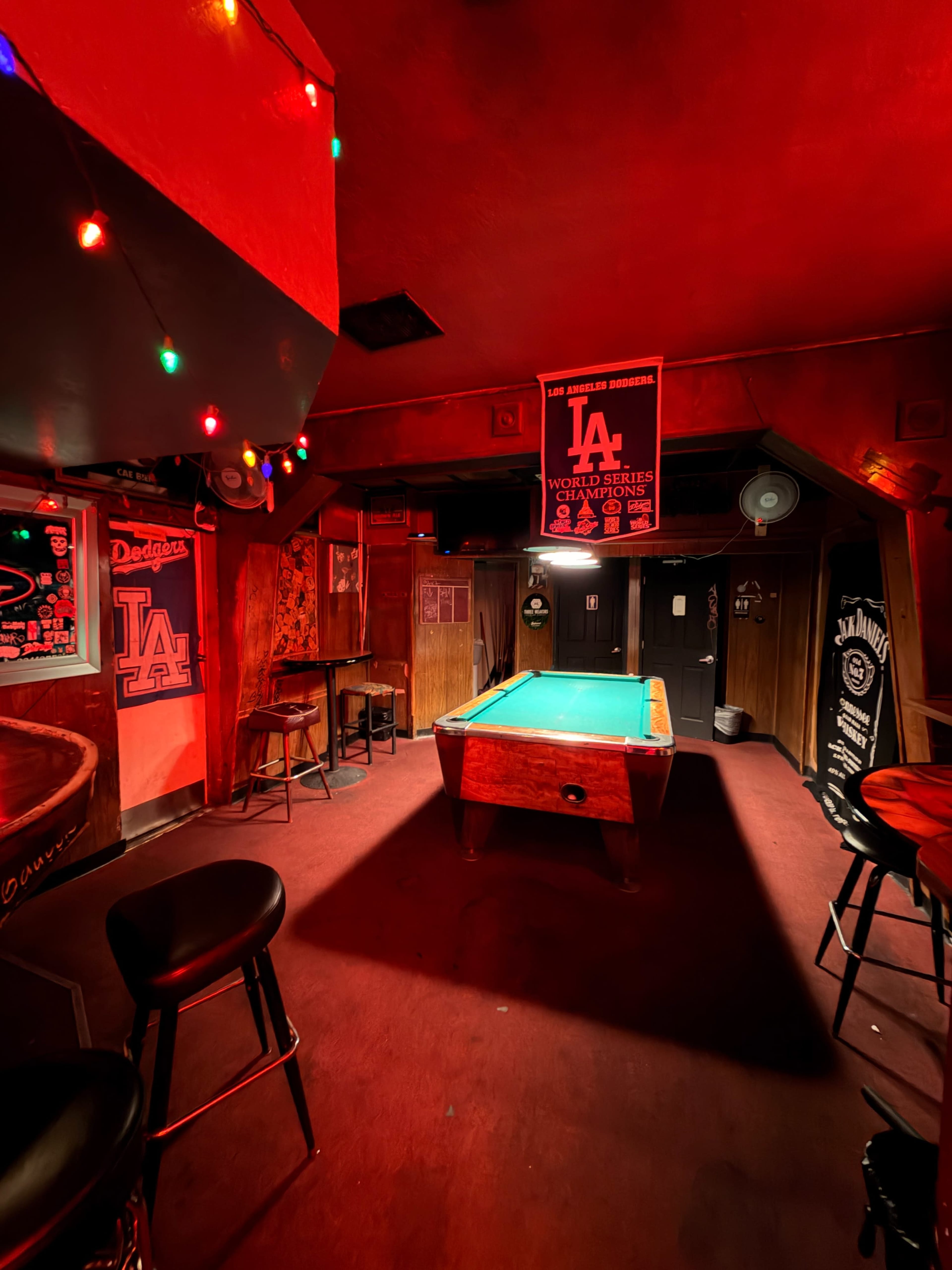 The image shows a dimly lit bar room with a pool table in the center, adorned with colorful lights and sports memorabilia on the walls.