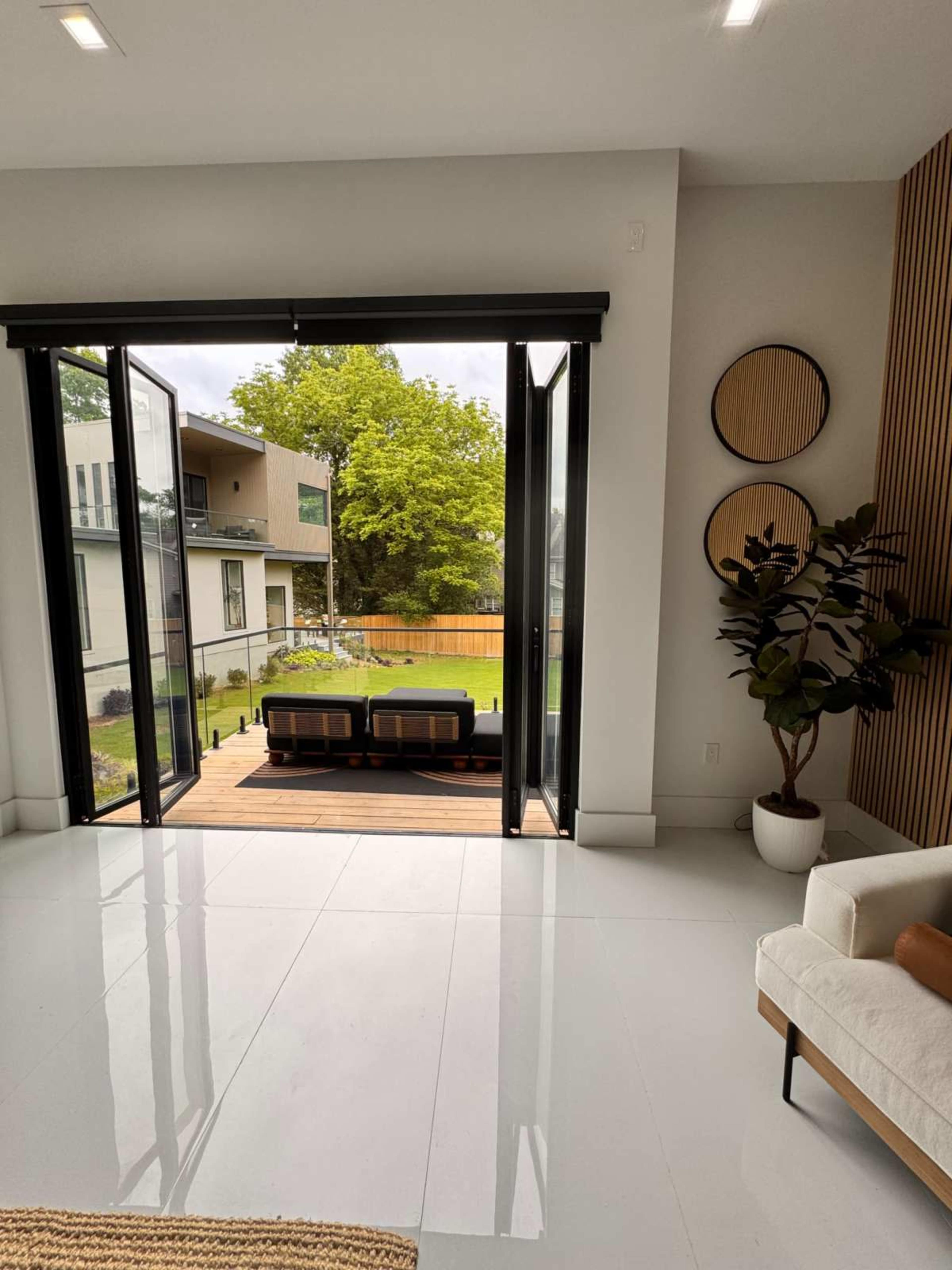 The image shows a spacious interior with large open doors leading to a patio area and a green yard surrounded by buildings.