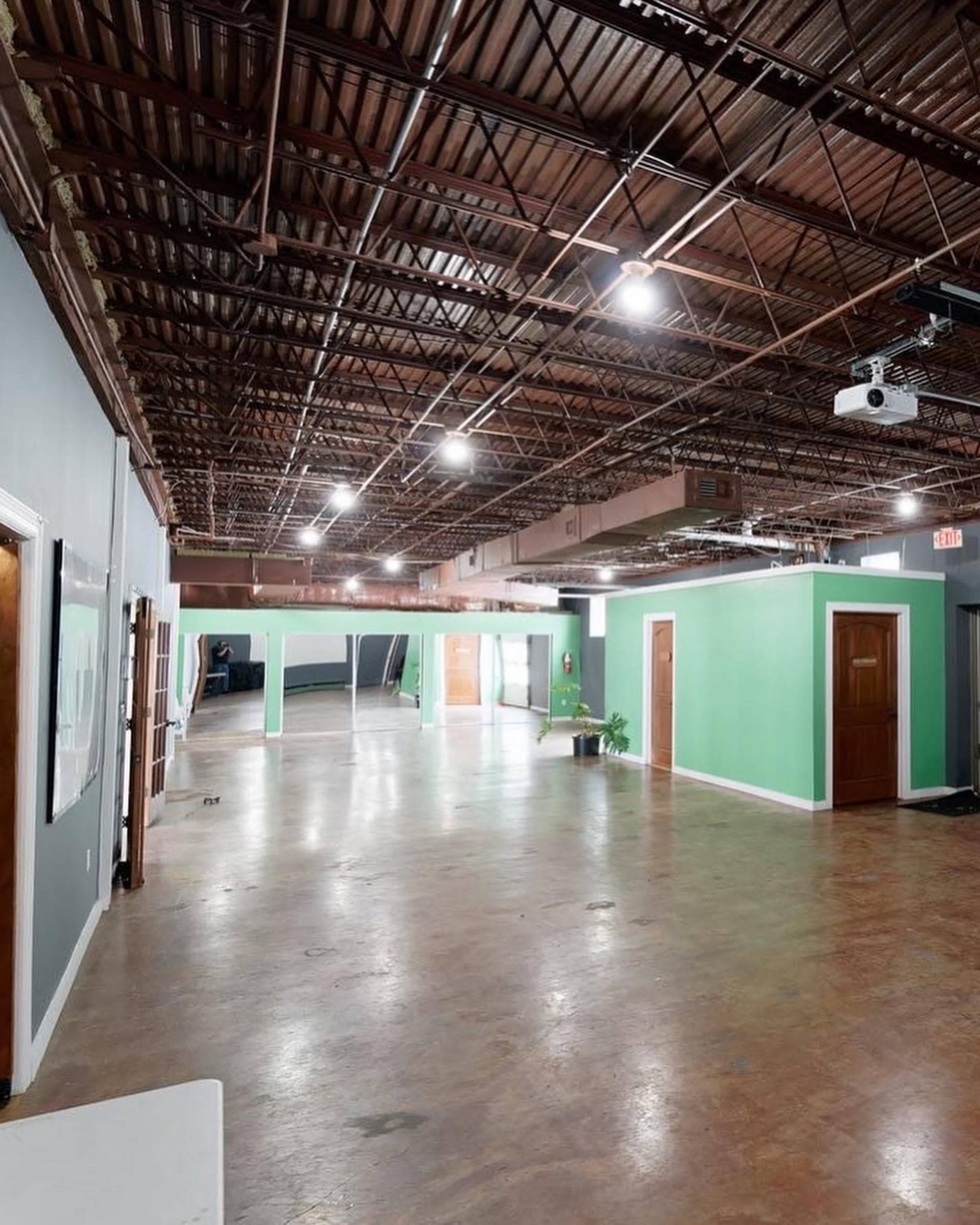 The image shows a spacious interior with a high ceiling, featuring green-painted walls, several doorways, and a polished concrete floor.
