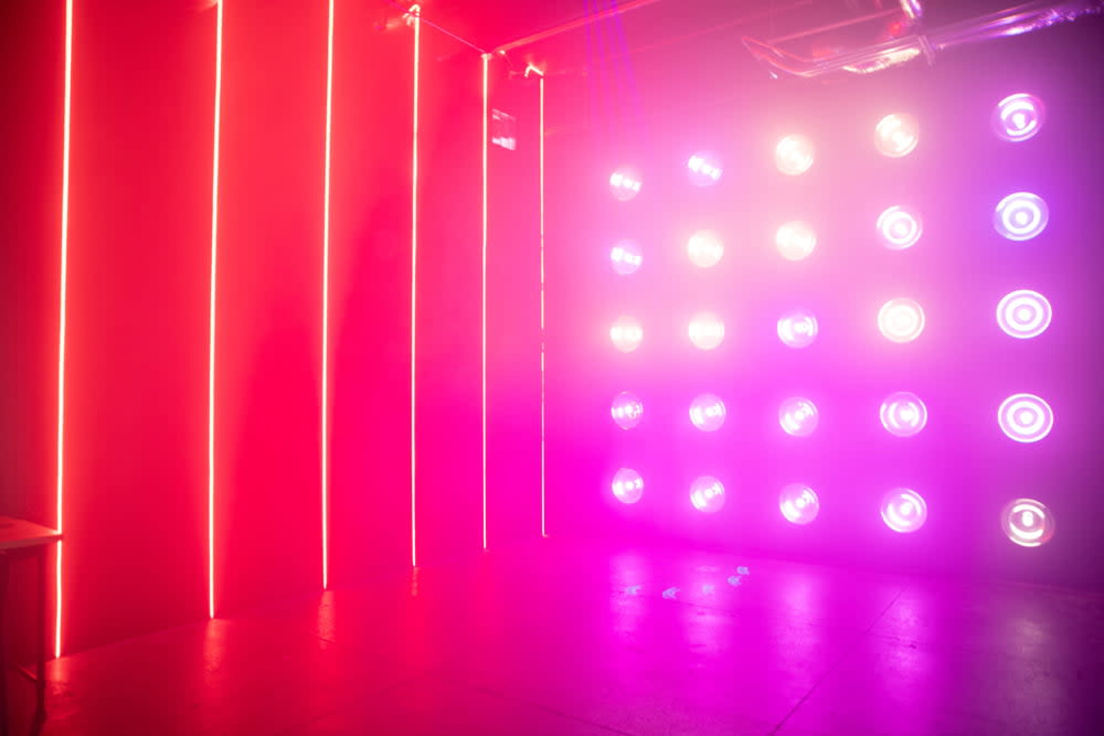 The image features a dimly lit room with vibrant pink and purple lighting, including vertical light strips and circular light fixtures on the walls.