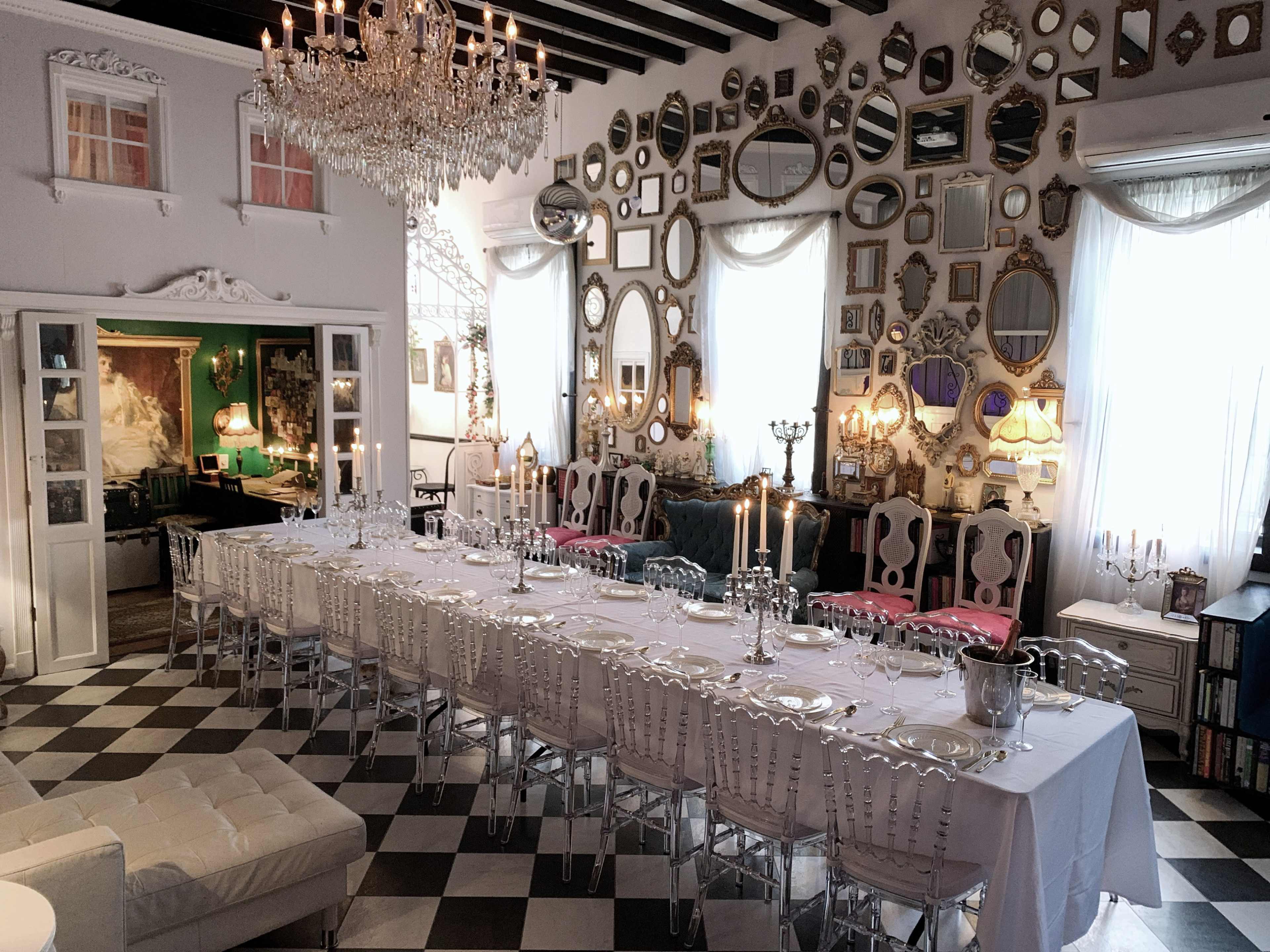 A long dining table is set in a room with a black and white checkerboard floor and a wall covered in various ornate mirrors.
