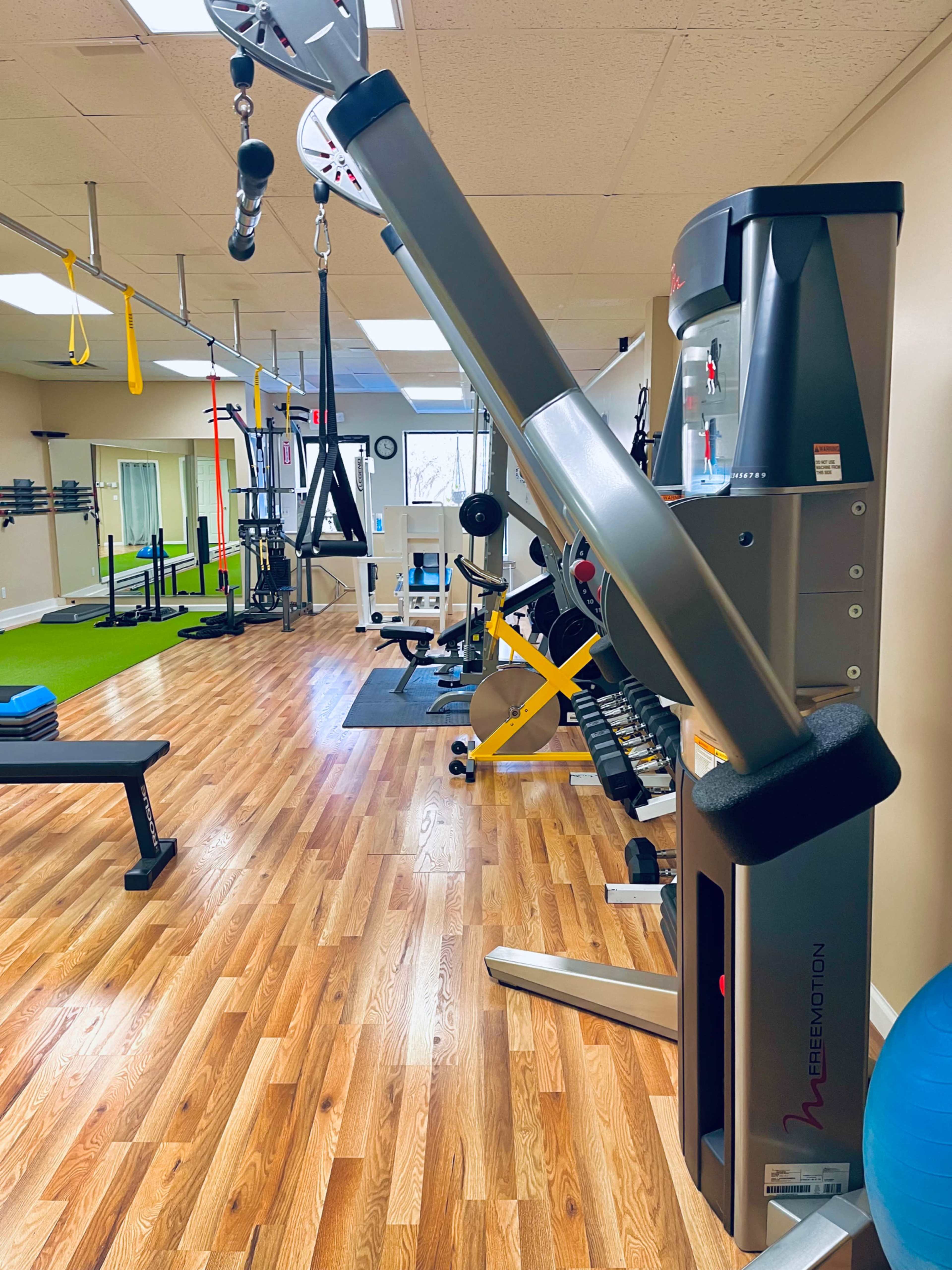 A well-equipped gym interior featuring various exercise machines, weights, and training equipment on wooden flooring.