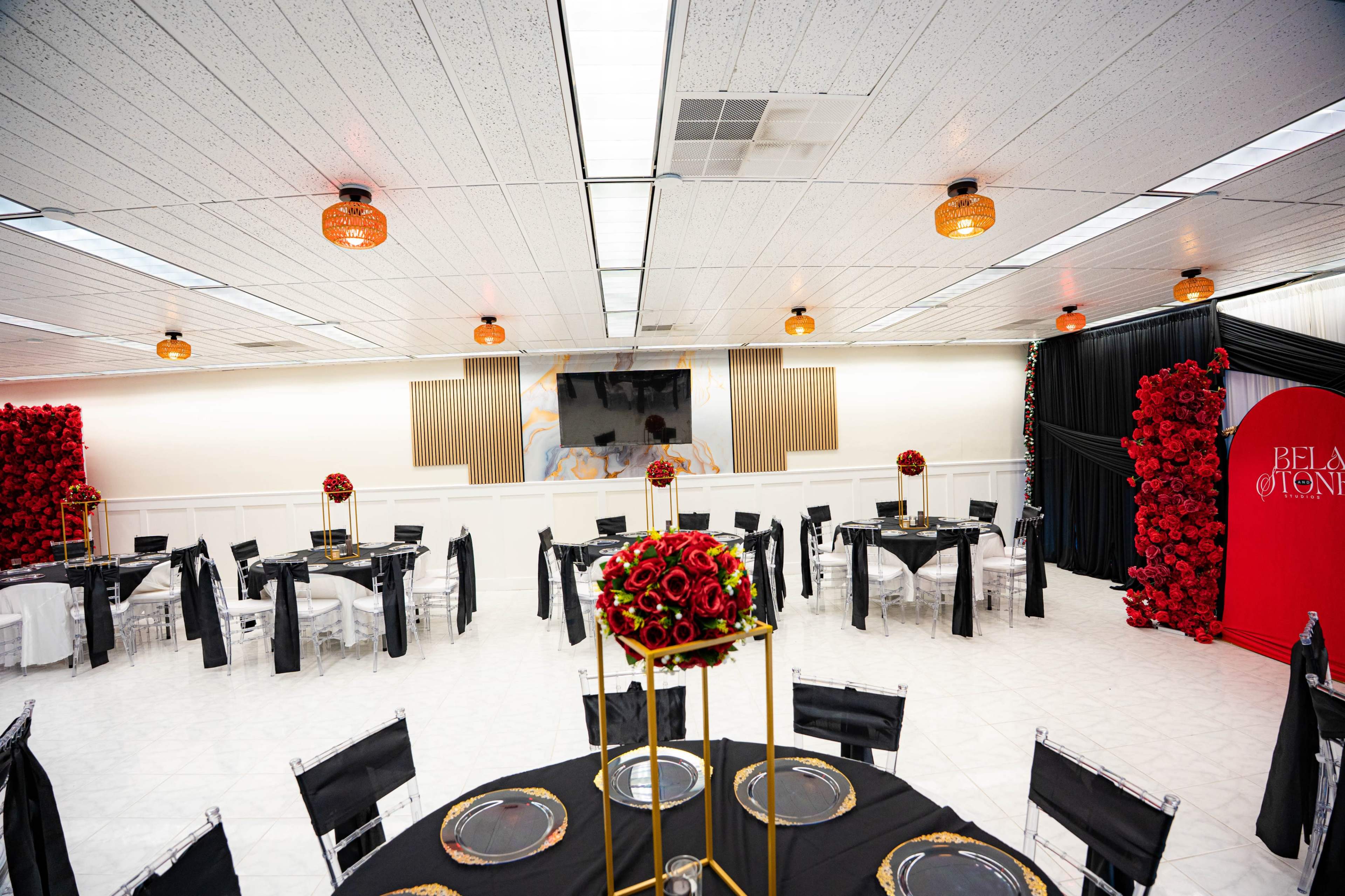A banquet hall is decorated with black and white table settings, floral centerpieces, and red accent walls featuring arrangements of roses.