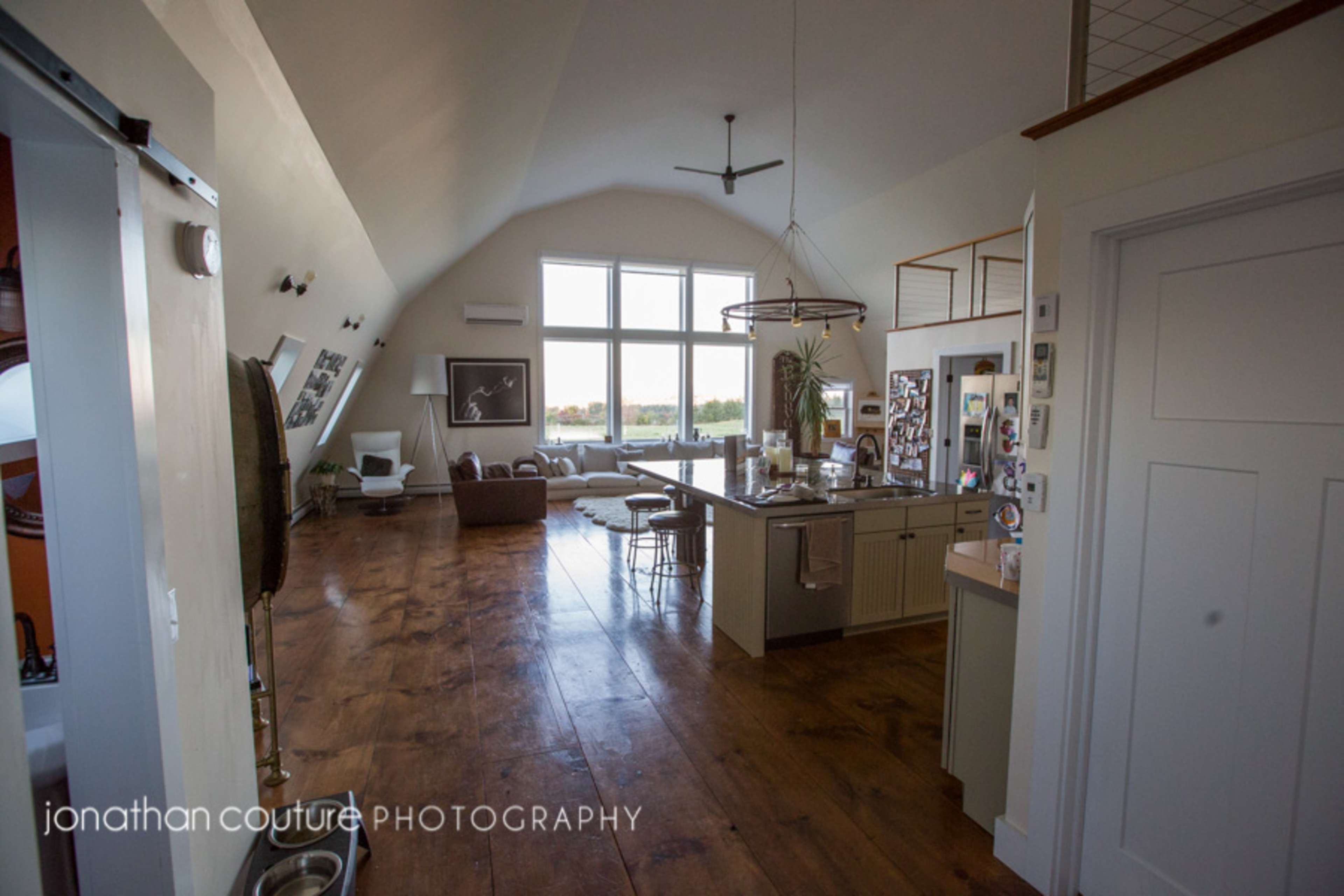 A spacious, modern living area with large windows, a kitchen island, and a seating area featuring a couch and armchairs.