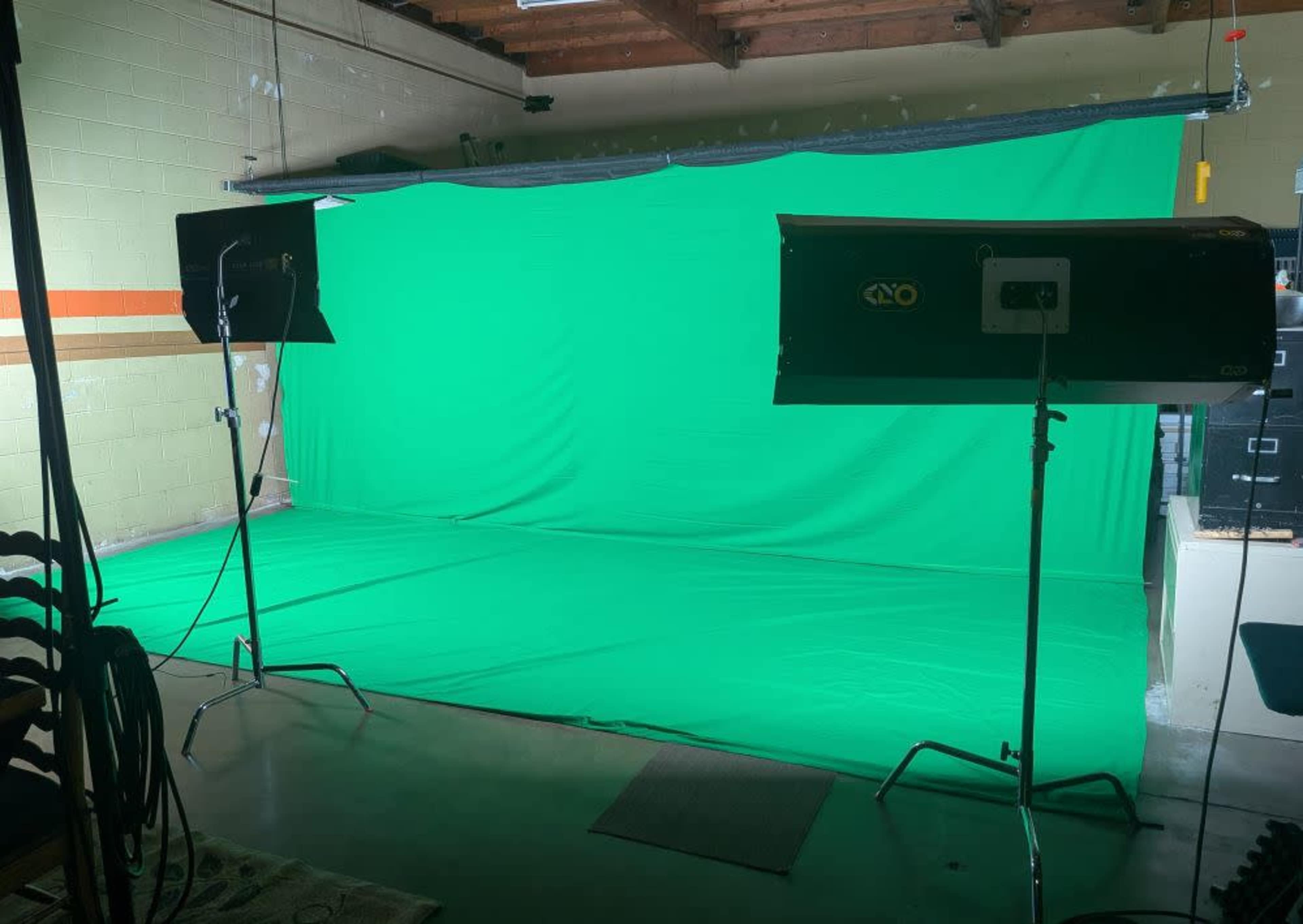 The image shows a room with a green backdrop set up for video or photography, flanked by two studio lights.