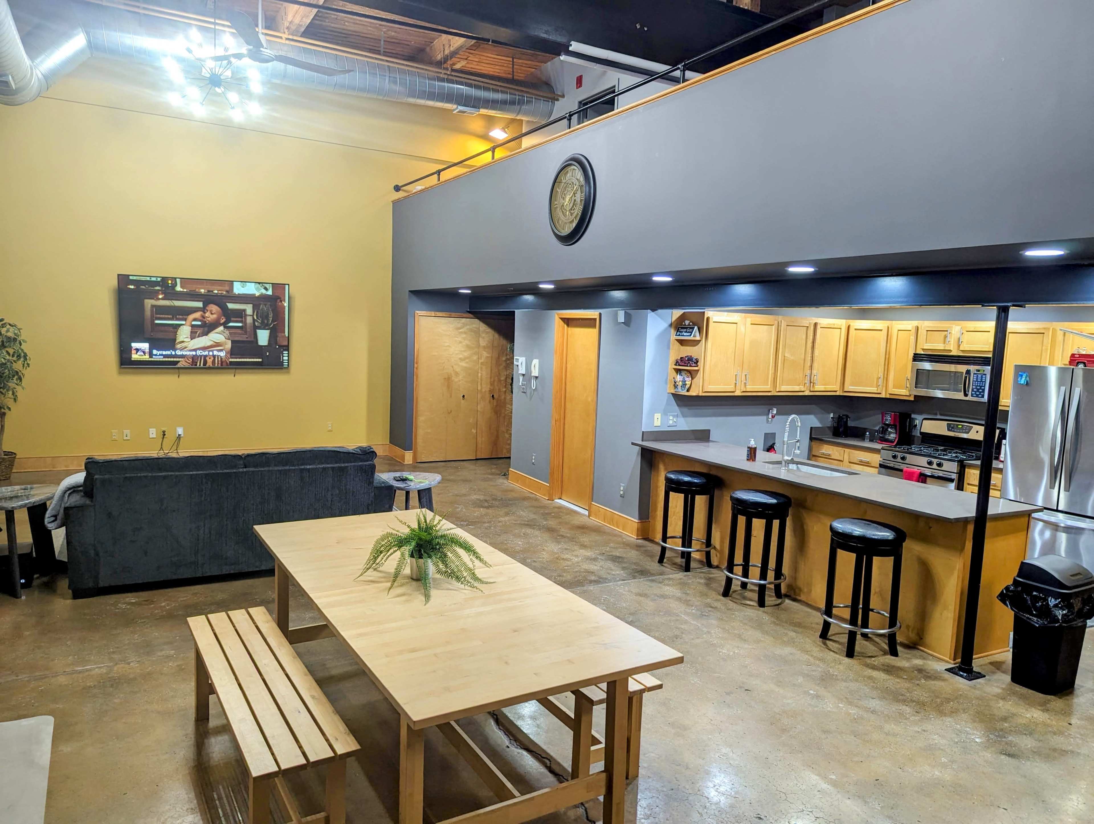 A spacious, modern living area featuring a kitchen with wooden cabinets, a dining table, and a seating area with a sofa.