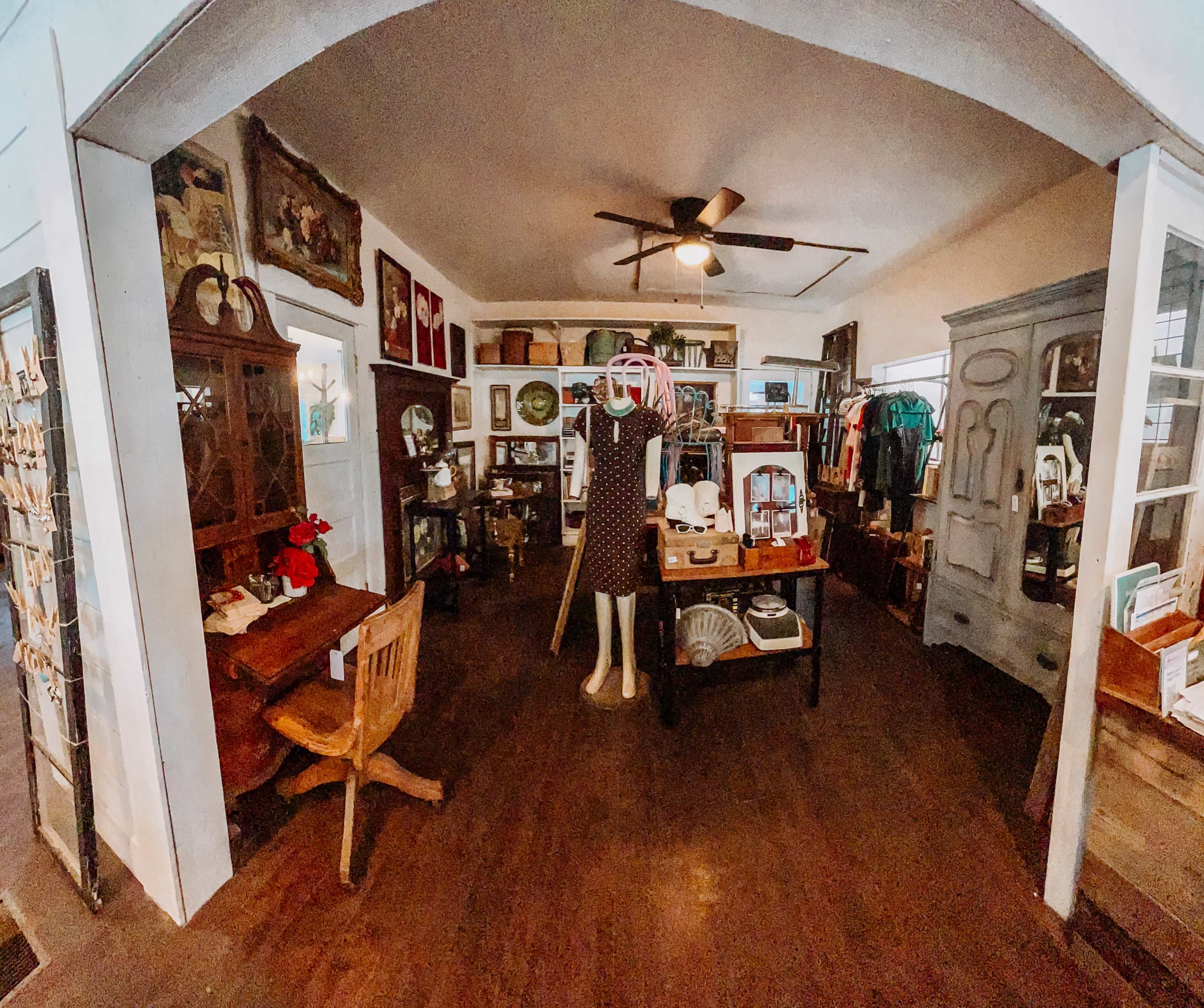 The image depicts a vintage shop interior featuring wooden furniture, decorative items, and clothing displayed on mannequins and tables.