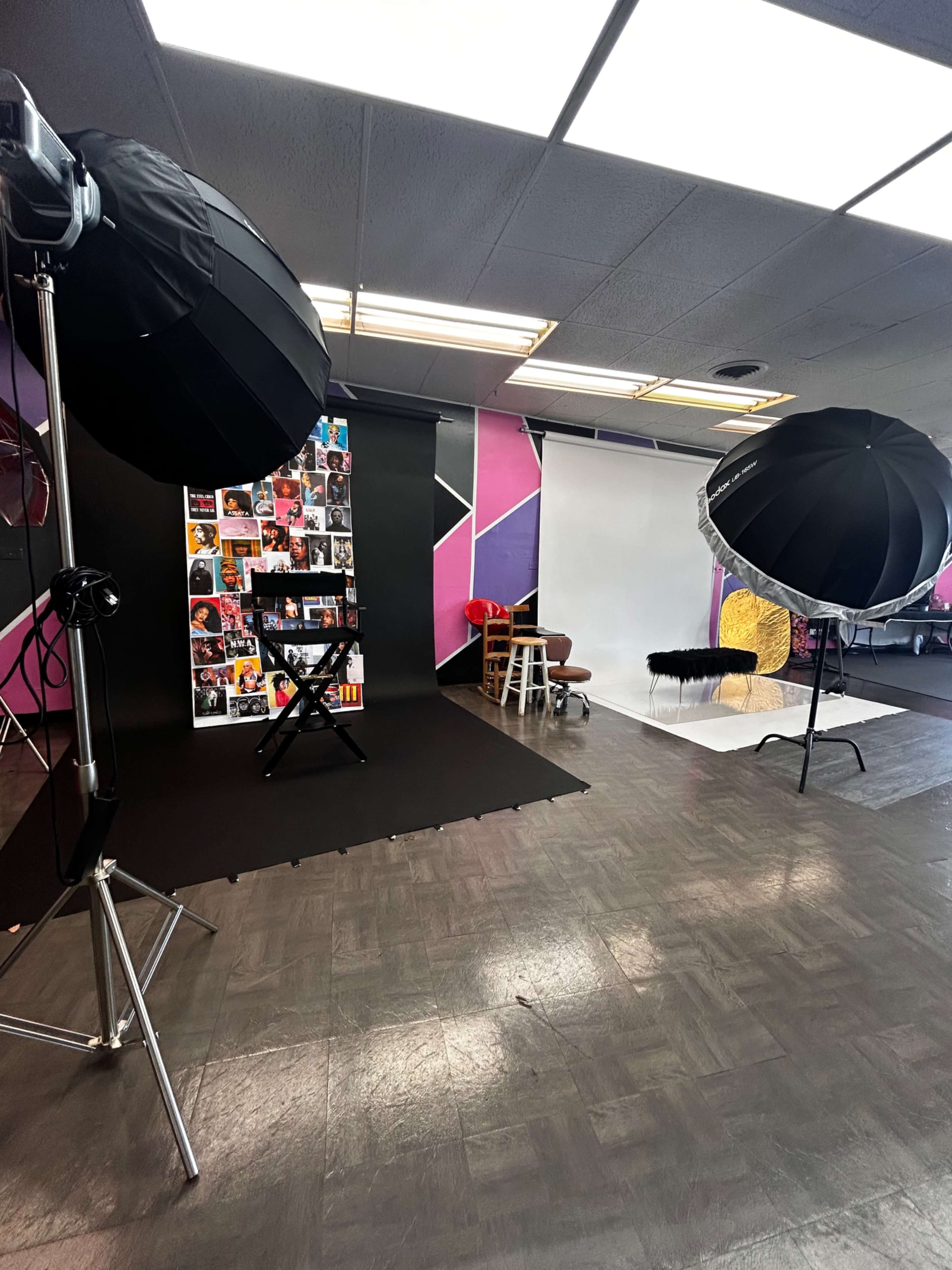 The image shows a photography studio equipped with large softbox lights, a backdrop displaying various images, and a white seamless backdrop in a colorful environment.
