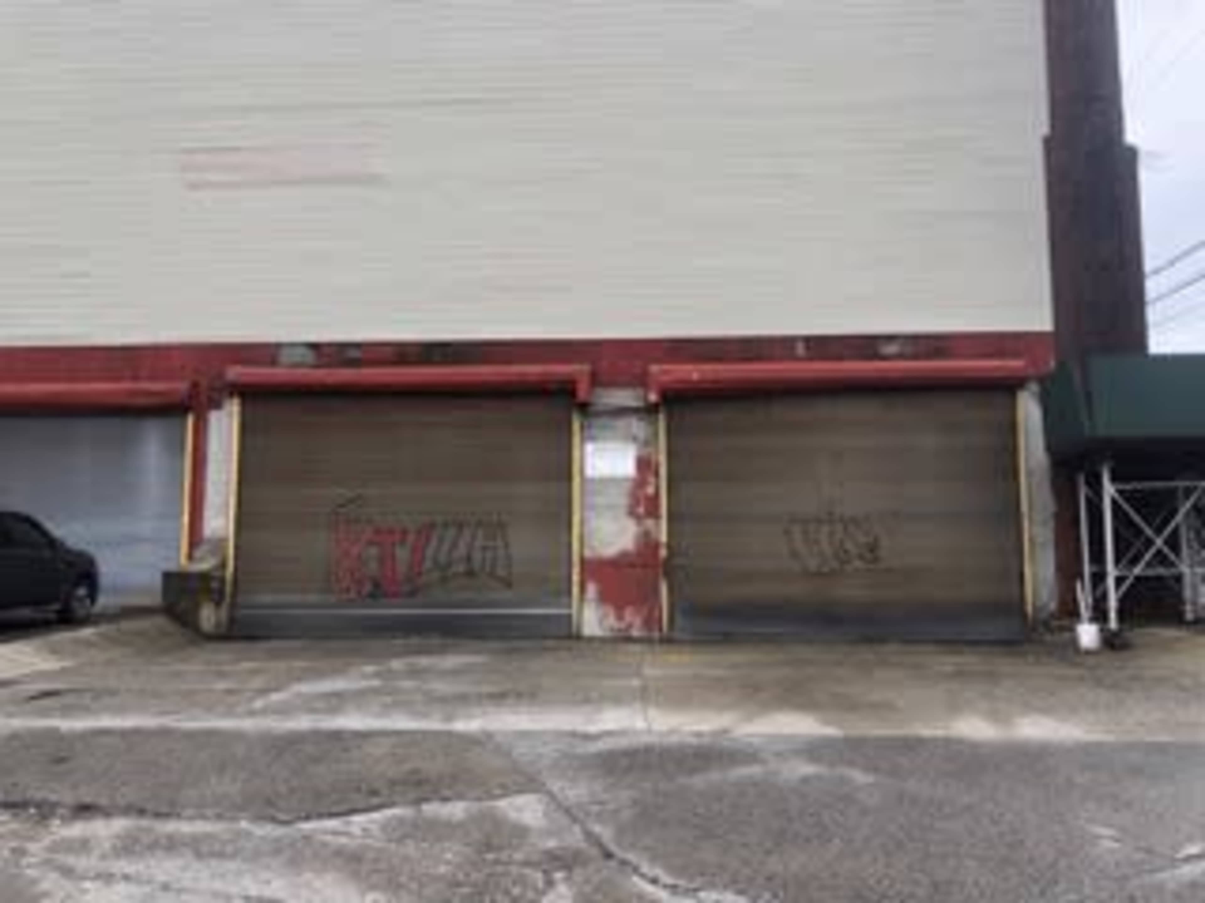 The image shows a building with two large, closed garage doors, each displaying graffiti, in an urban setting.