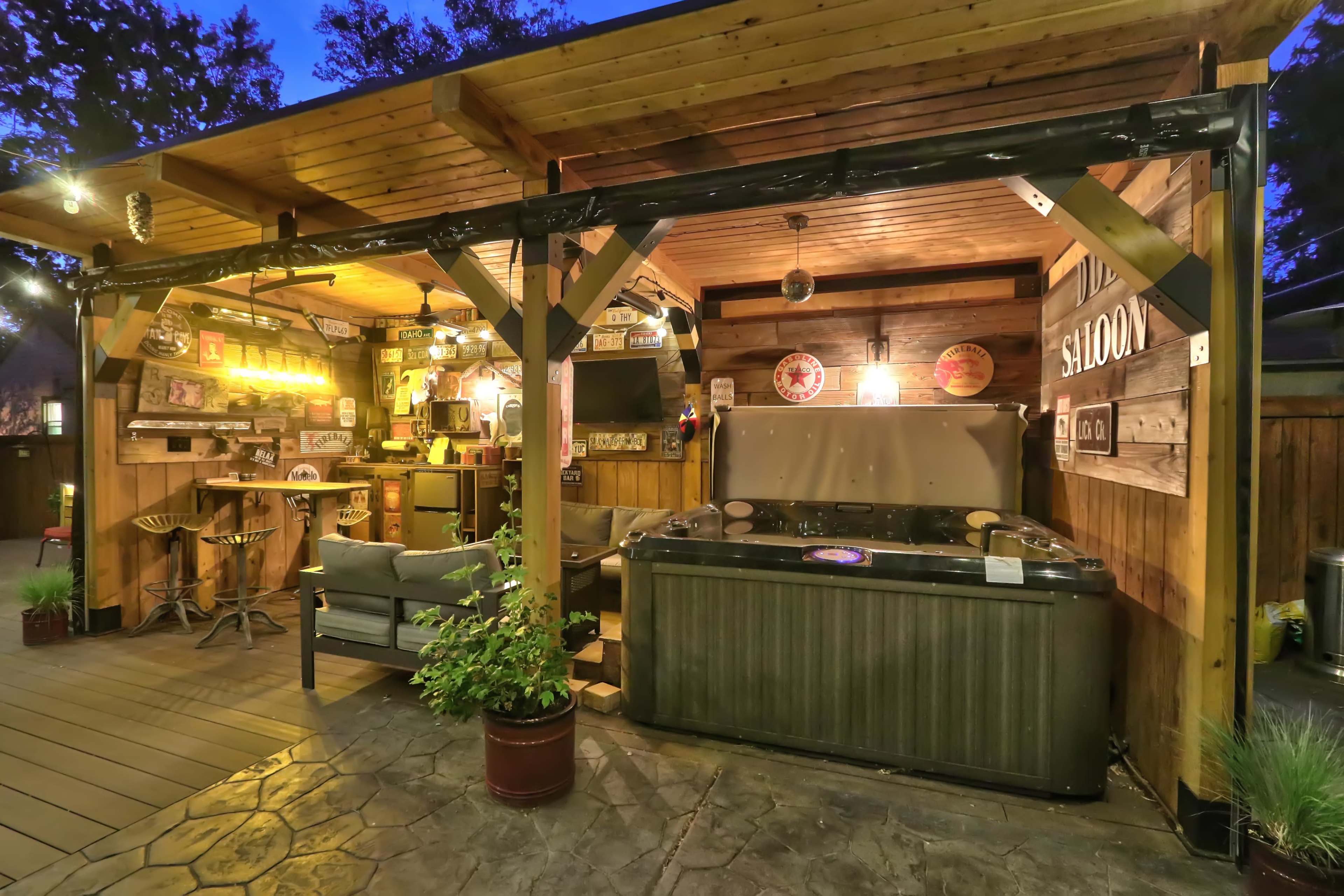 A wooden gazebo area featuring a hot tub, seating, and bar with decorative lights.