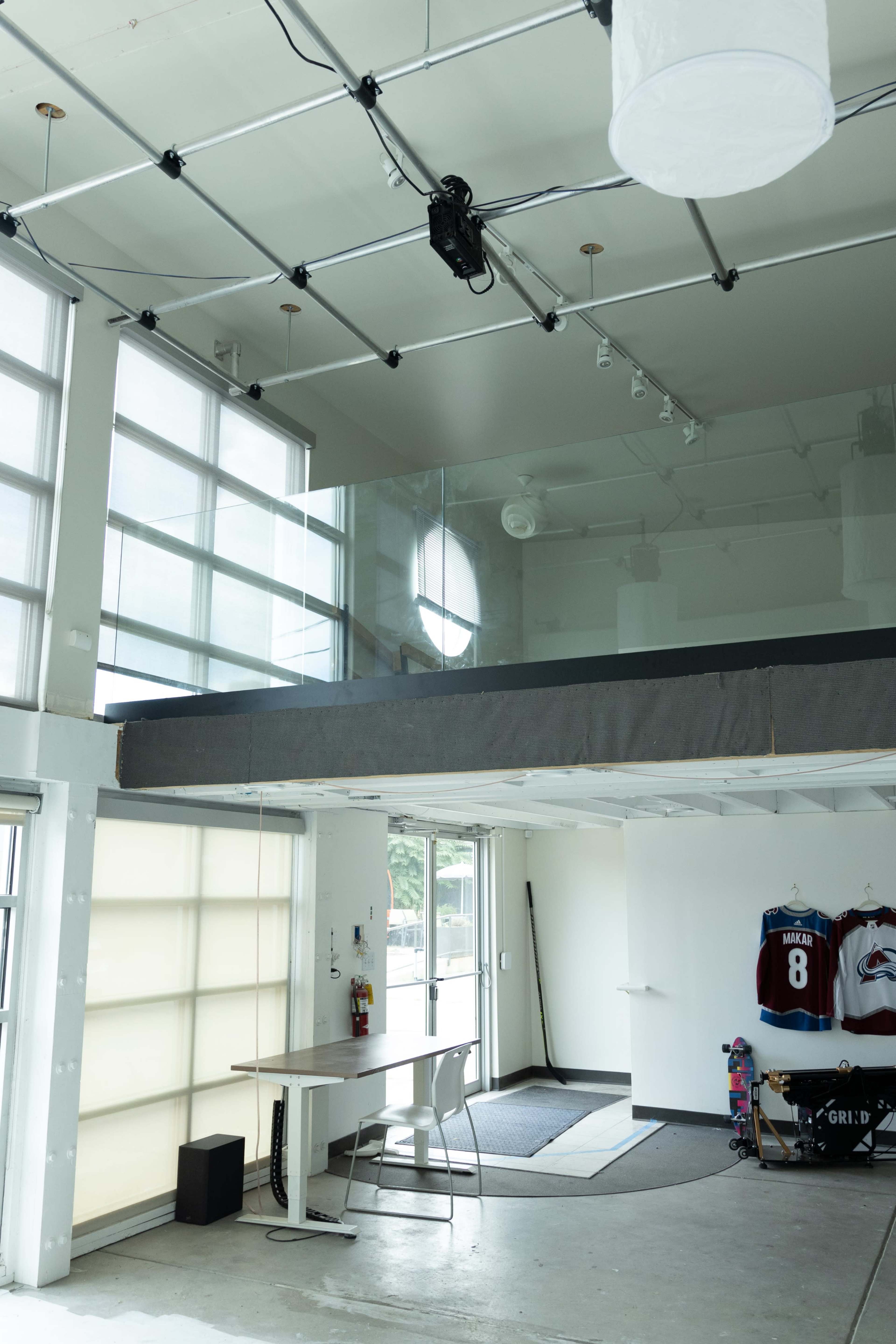 A modern, open space with a lofted area, large windows, and a minimalist design featuring a table and equipment on the floor below.
