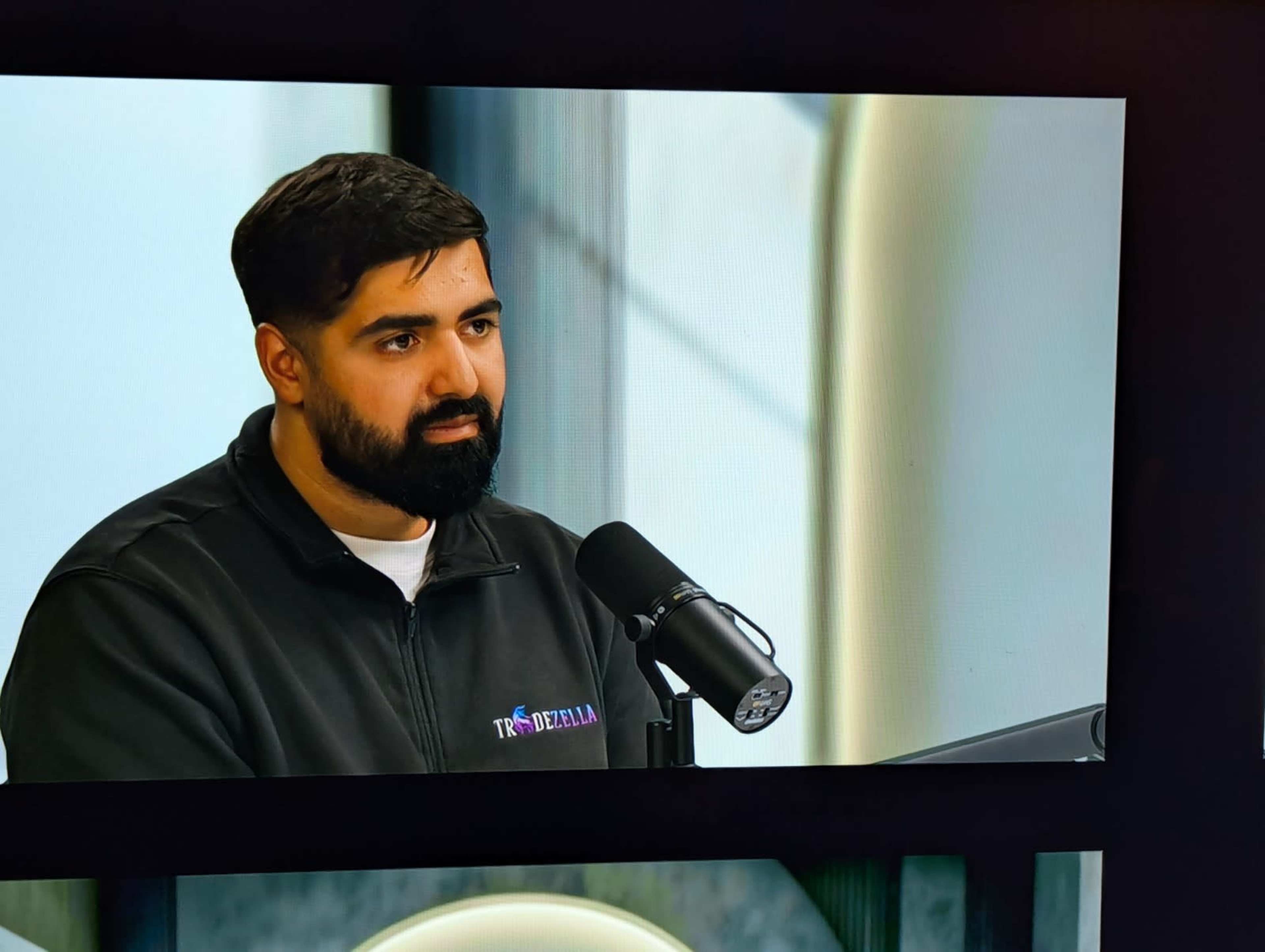 A man with a beard is speaking into a microphone during a broadcast.