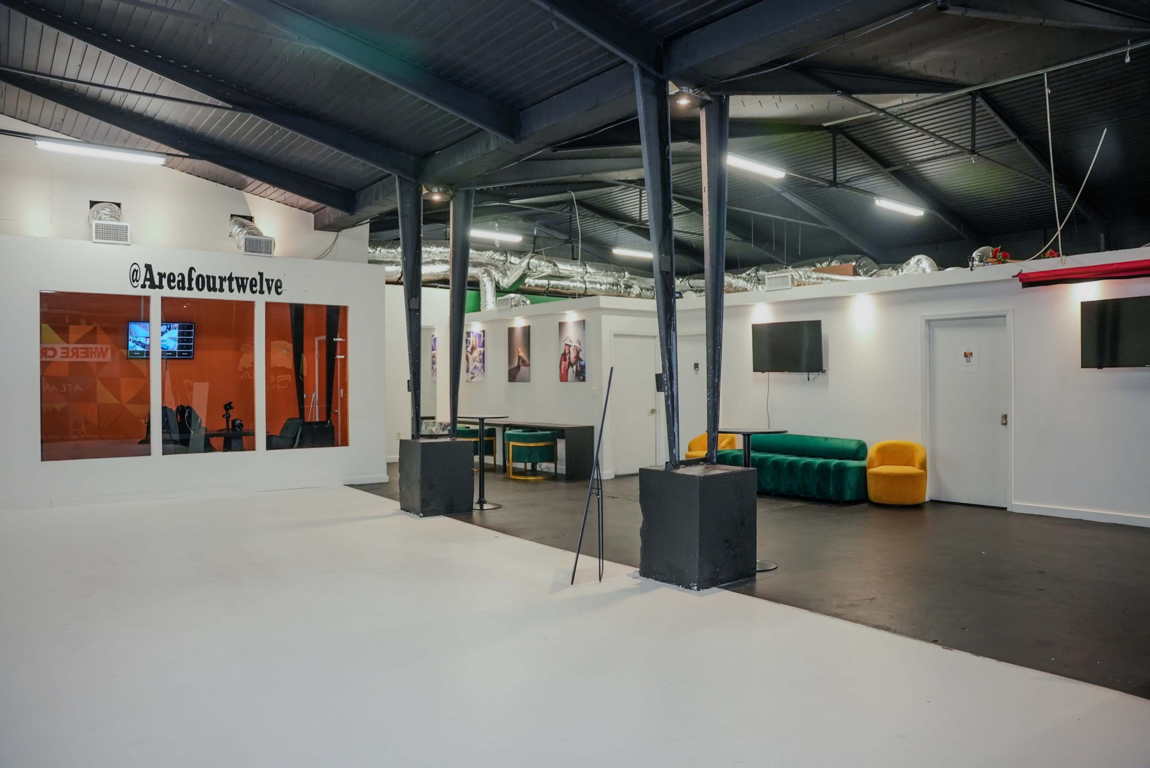 The image shows a spacious, modern indoor area with sections for seating and entertainment, featuring white walls, a black ceiling, and various furniture arrangements.