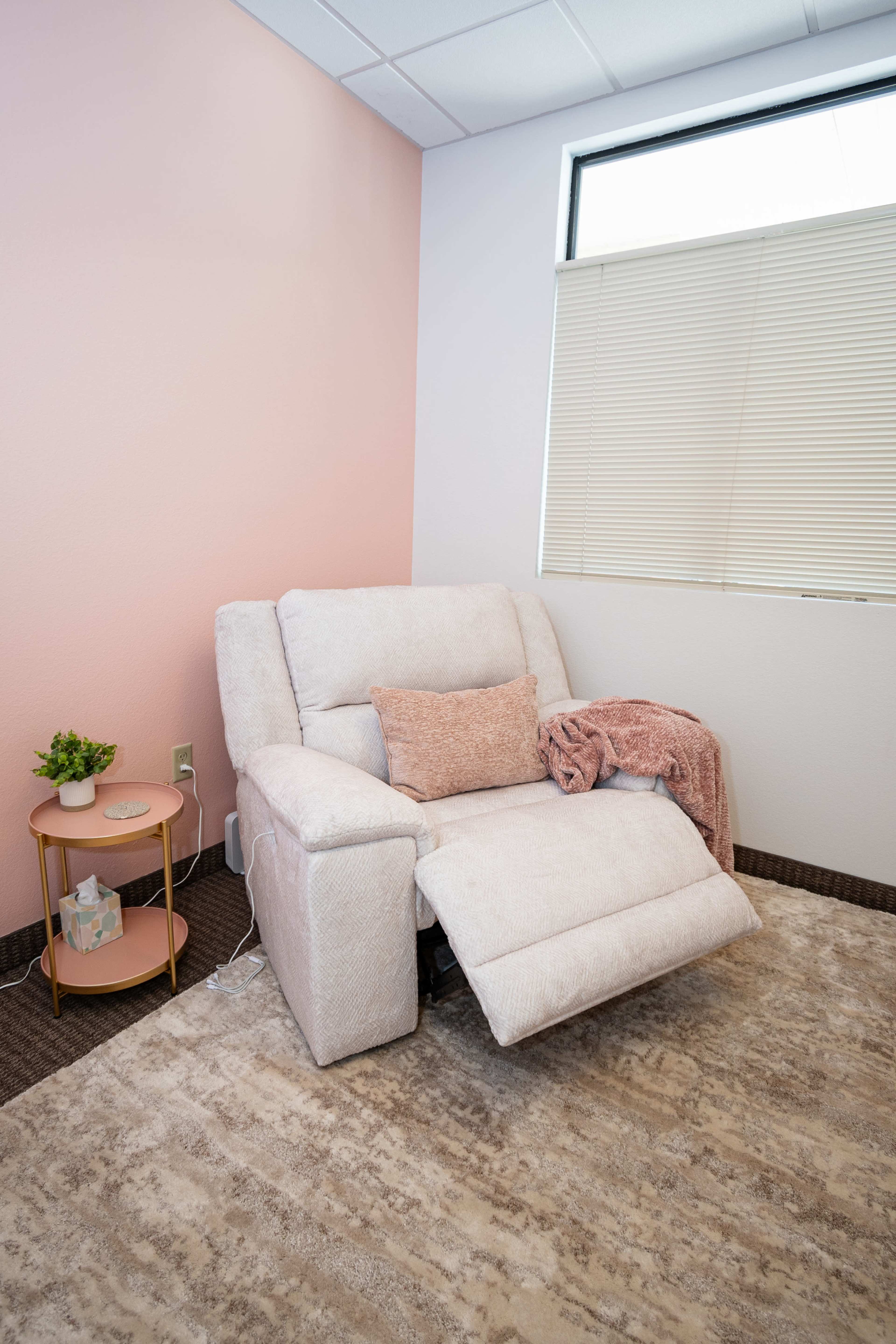 The image shows a cozy corner of a room featuring a recliner chair with a throw blanket and a small round side table next to it.