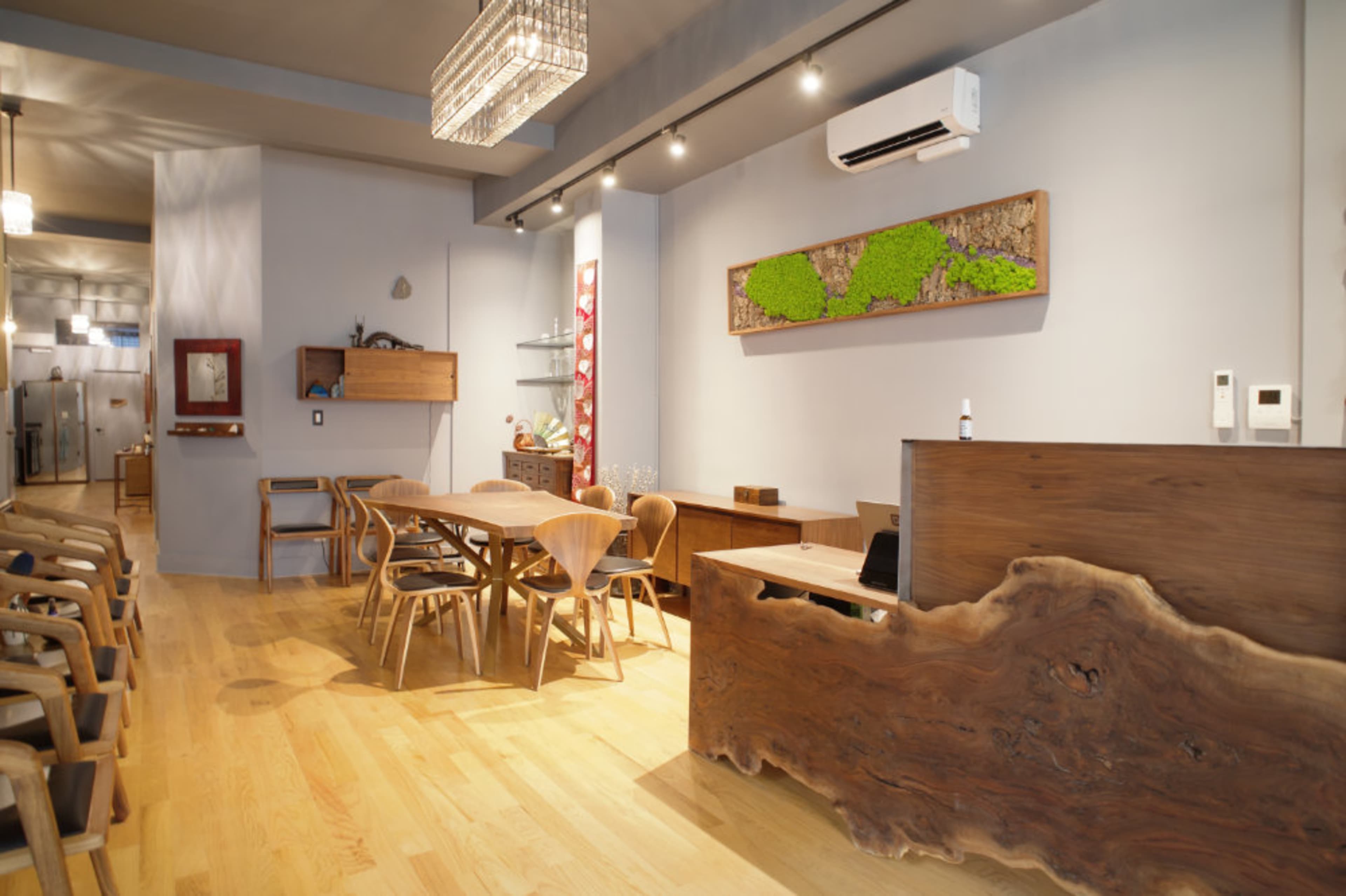 A modern interior features wooden furniture, including a dining table and chairs, with a sleek reception desk and wall-mounted decor.