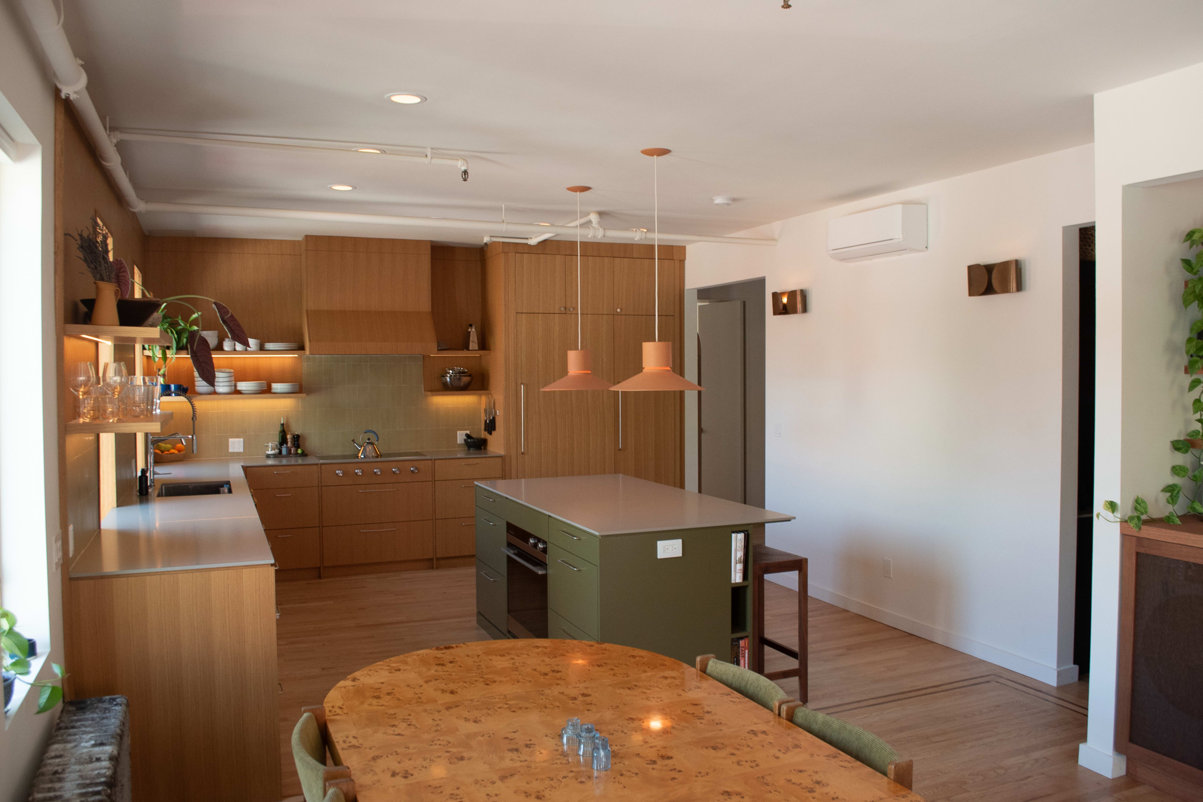 A modern kitchen features wooden cabinetry, an island with a green base, and an adjacent dining table.