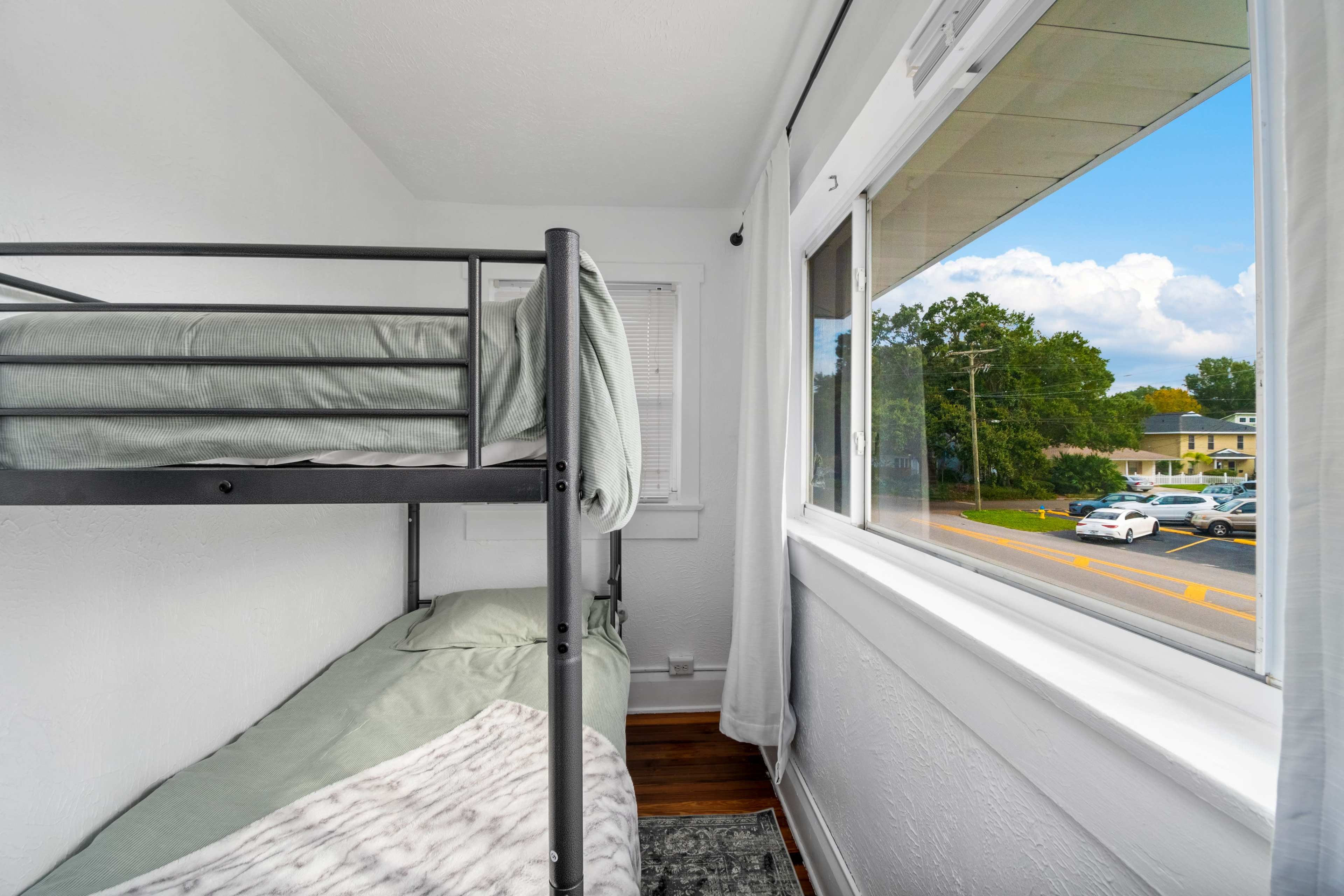 A small bedroom with a metal bunk bed and a window overlooking a street with parked cars.
