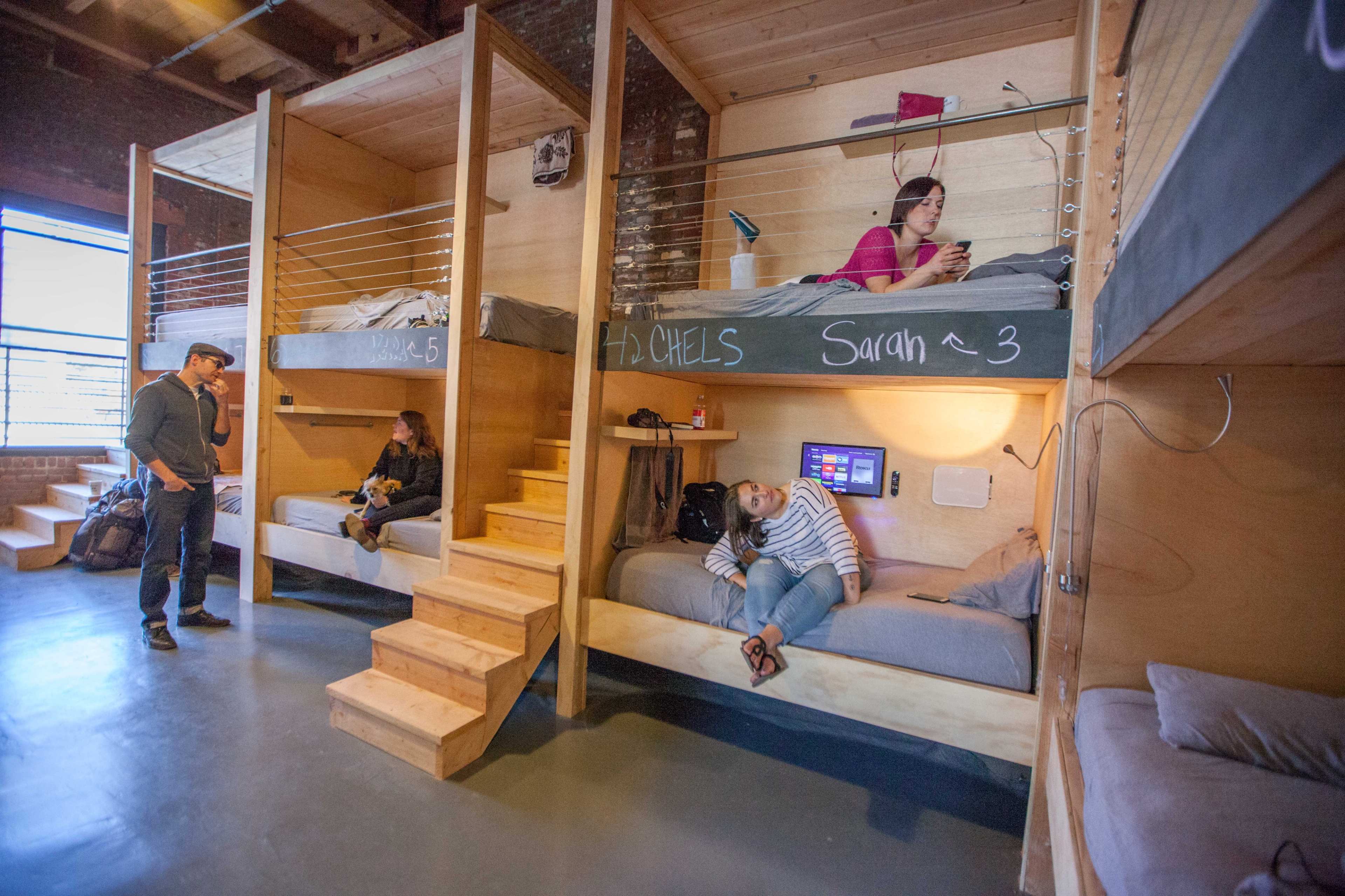 A shared dormitory with bunk beds, where two occupants are resting, one person is on a phone, and another is standing nearby.