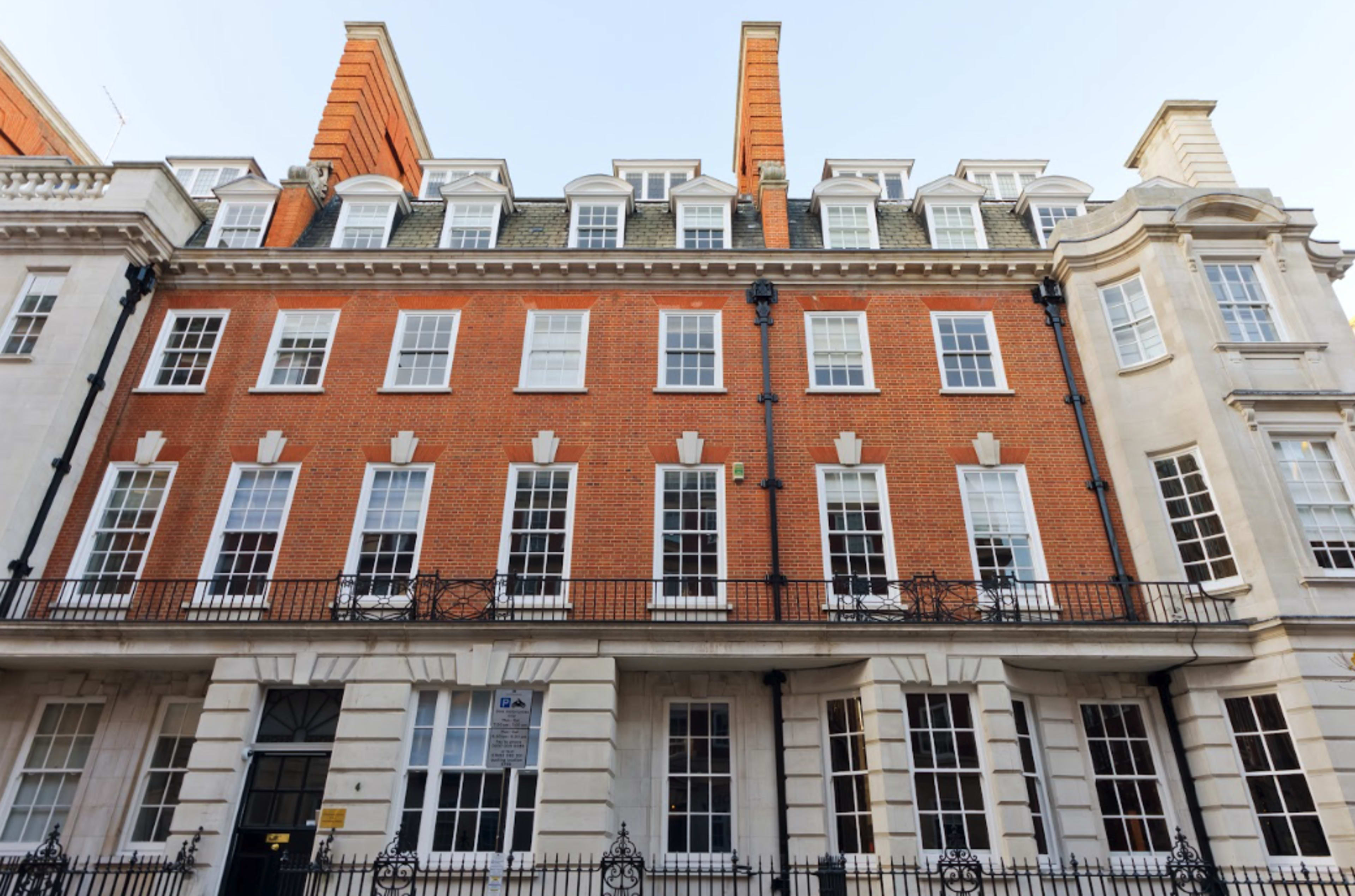 The image shows a classic red brick building with white window frames and decorative stonework, featuring multiple stories and a black wrought-iron railing.