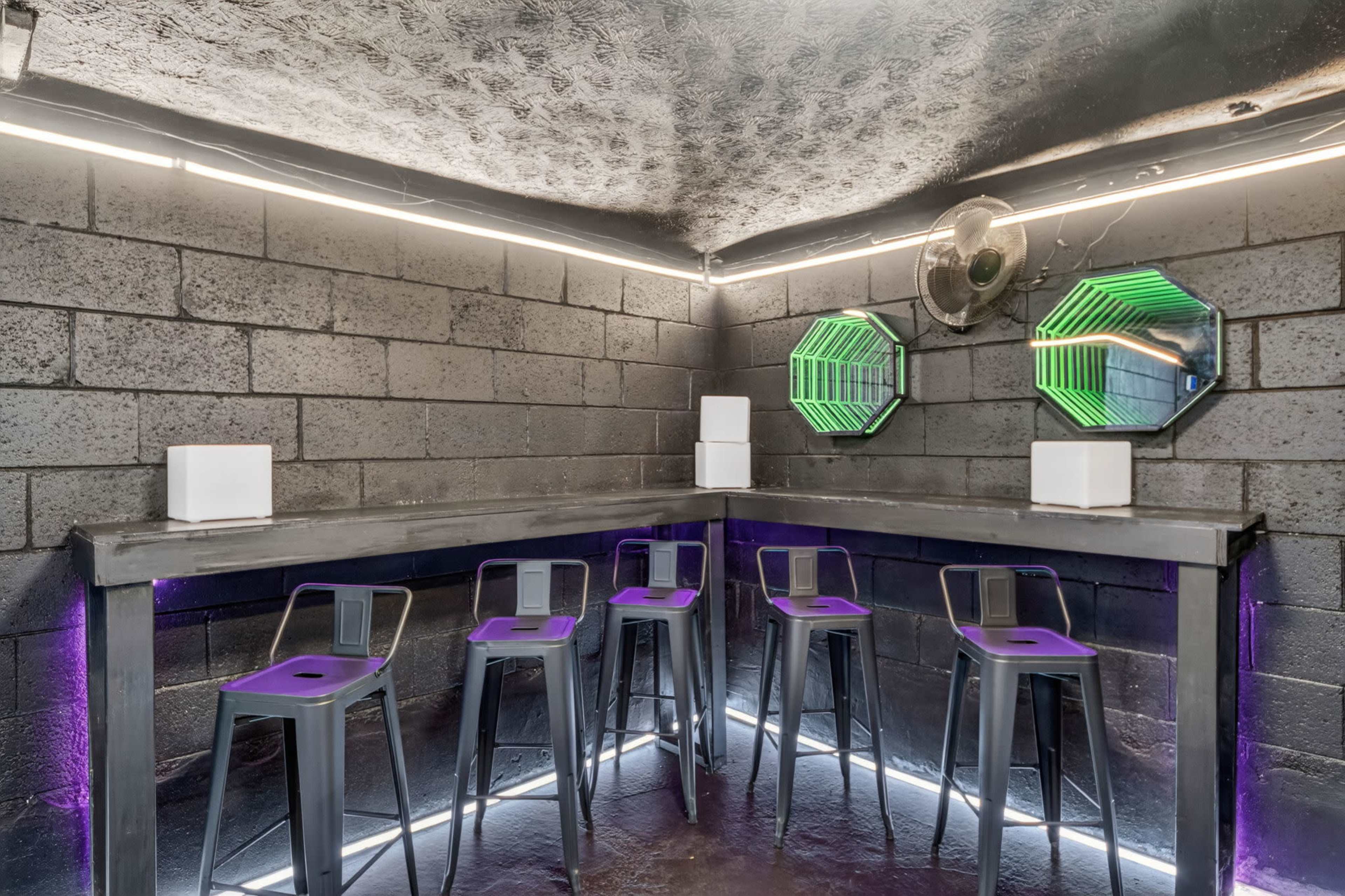 The image shows a modern bar area with metal stools and a sleek countertop illuminated by neon lights.