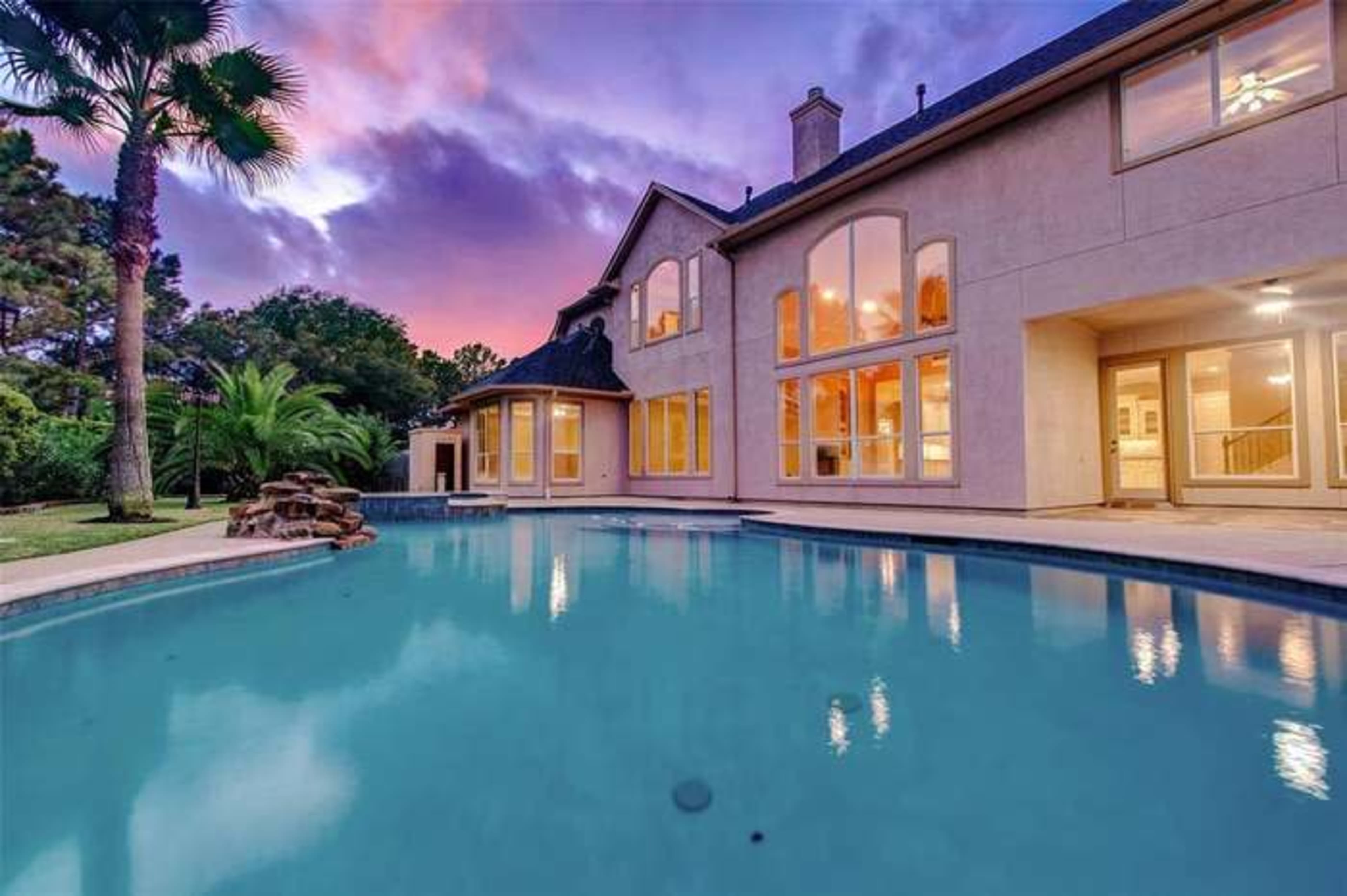 A backyard pool reflects the twilight sky next to a spacious house with large windows.