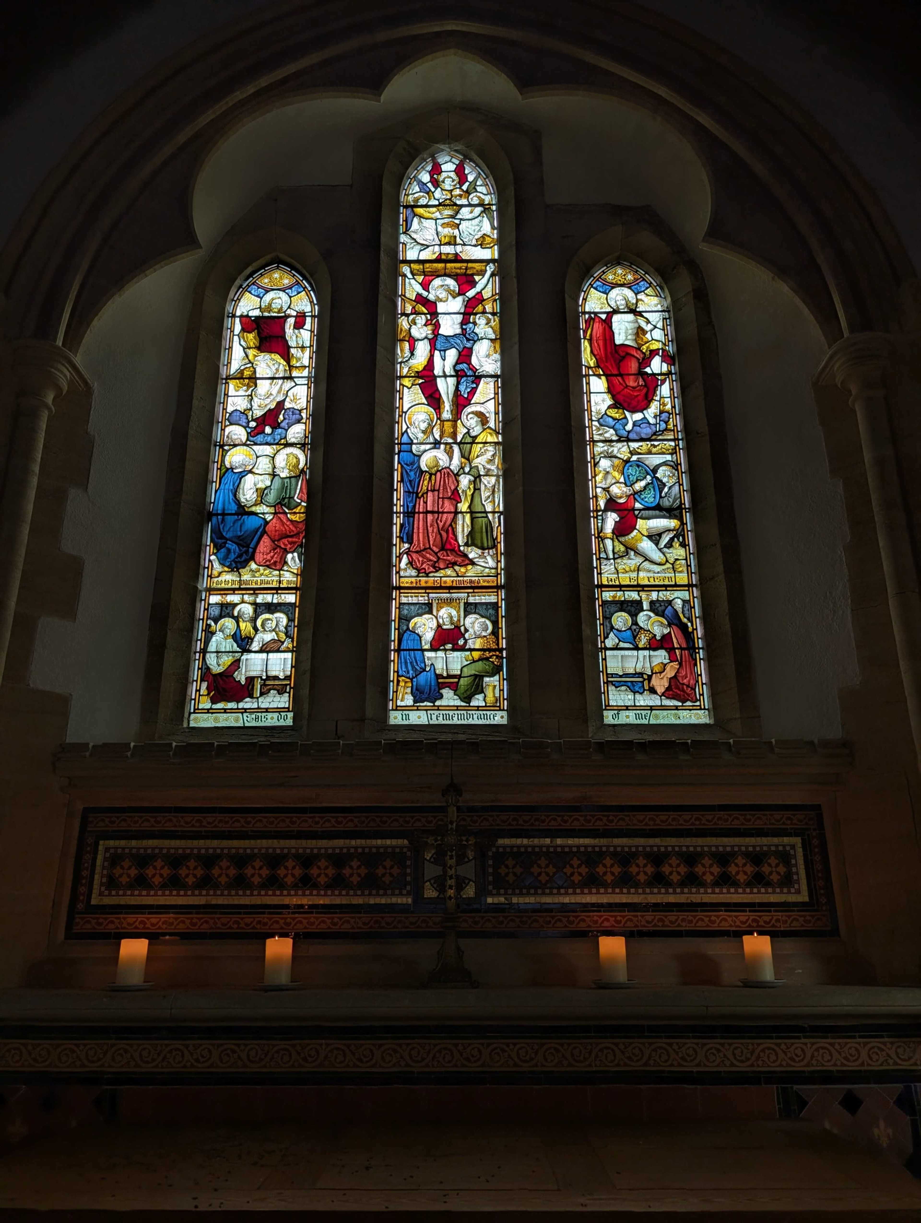 The image shows three large stained glass windows featuring biblical scenes, illuminated by soft interior light in a church setting.