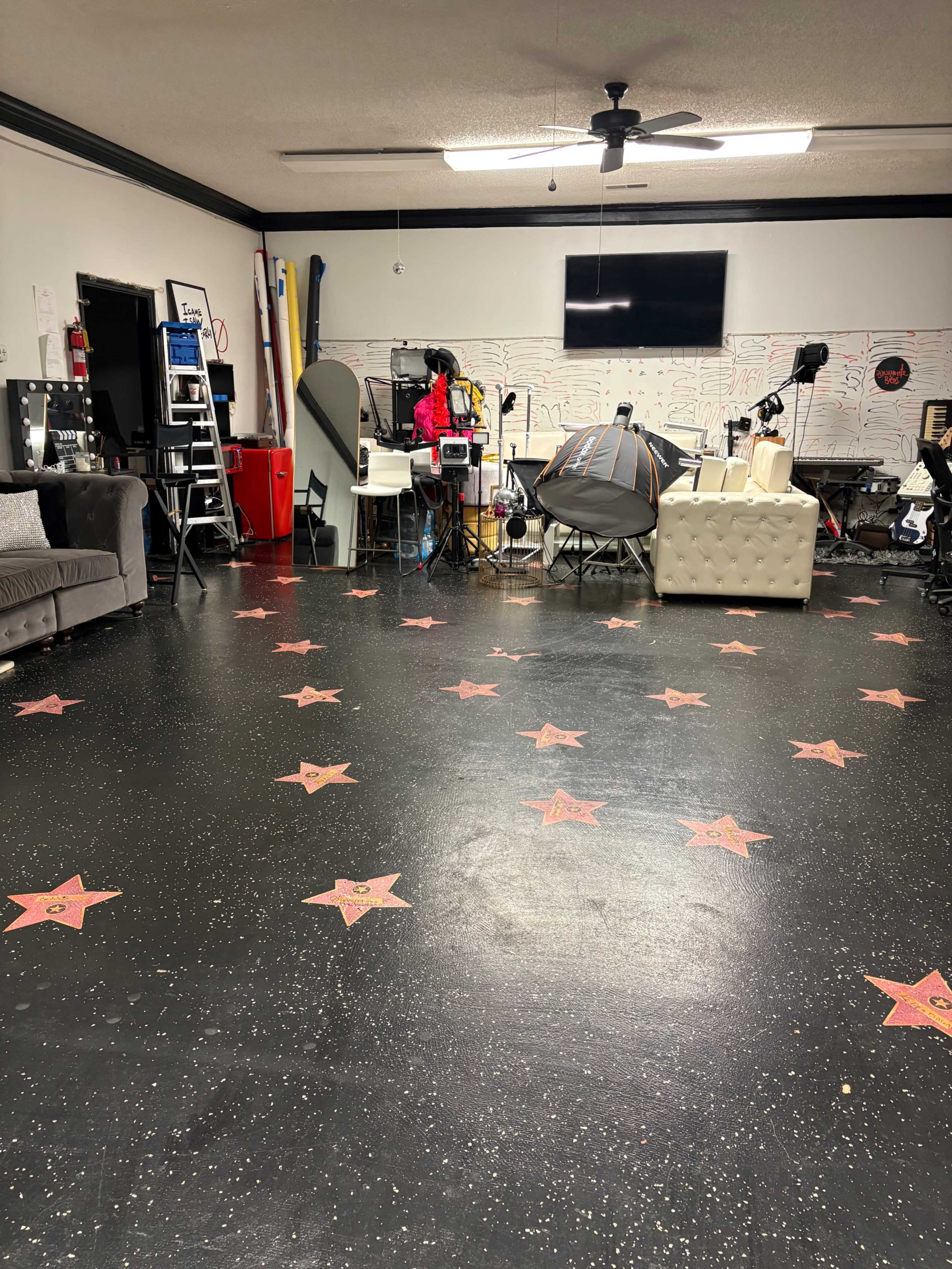 The image shows a spacious room with a black floor decorated with red star patterns, featuring various equipment and furniture set up for a filming or photography environment.