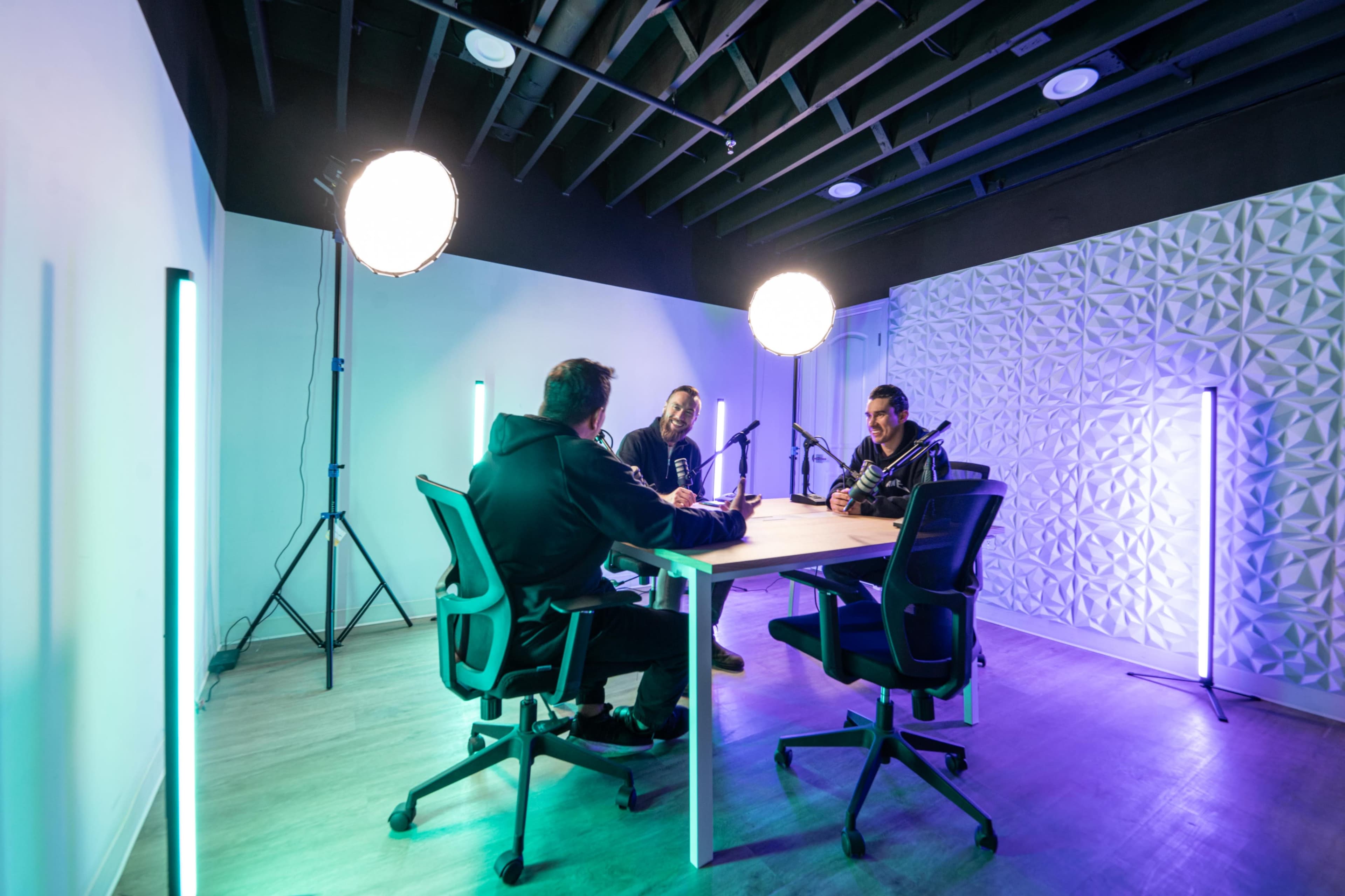 Three people are seated at a table in a well-lit modern room, with microphones positioned in front of them.