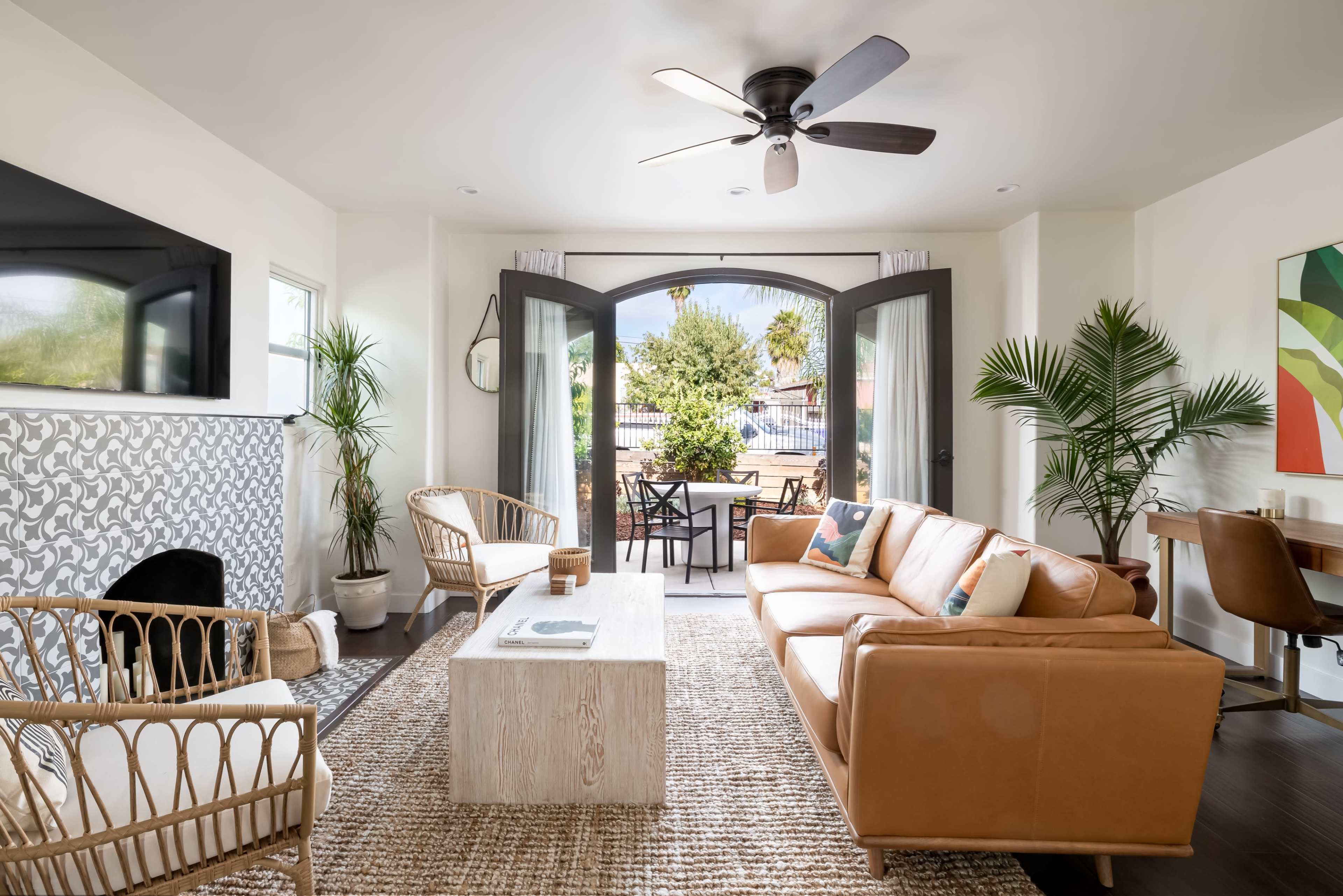 The living room features a leather sofa, wicker chairs, a wooden coffee table, and large arched doors leading to an outdoor patio.