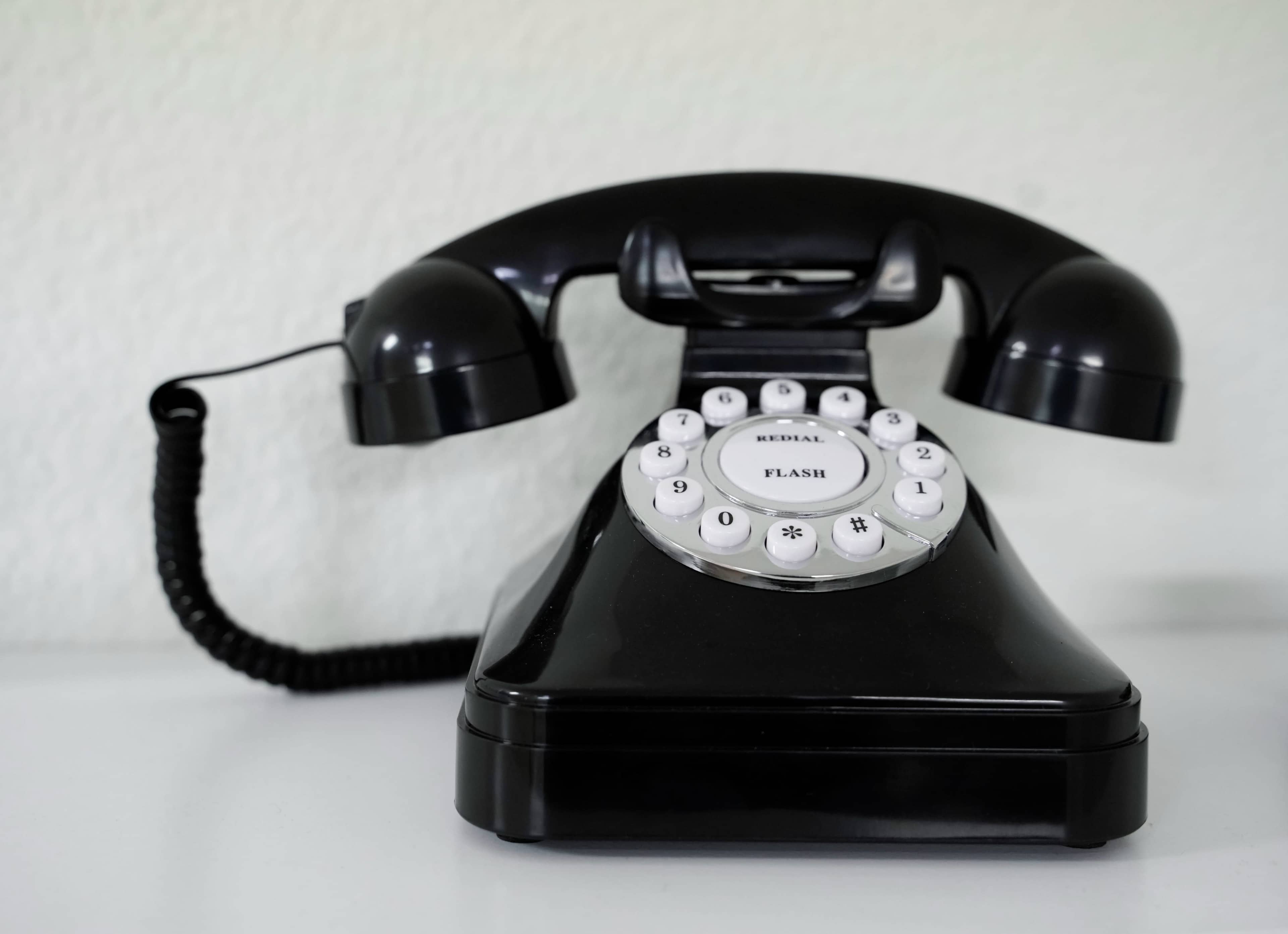 A black rotary telephone with a sleek design placed on a white surface.